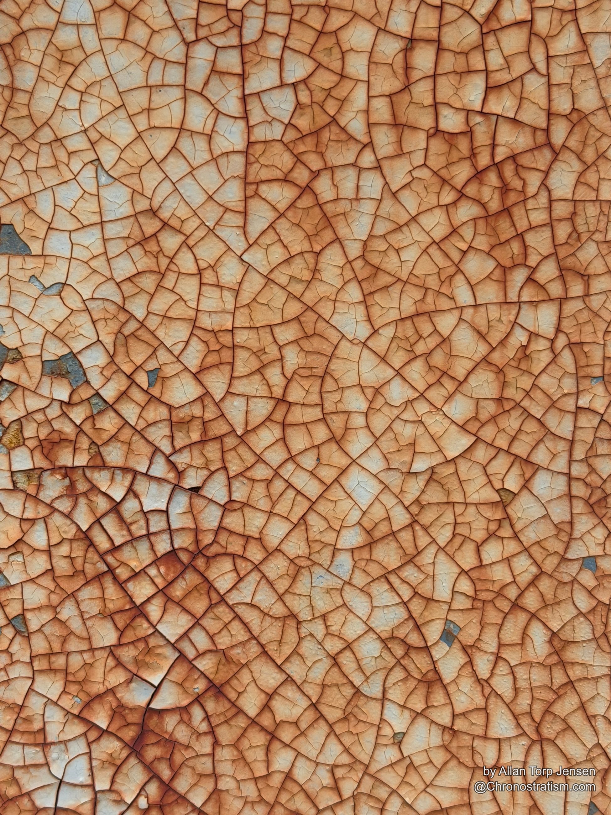 Fine alligator cracking radiates in circular fractures across rust-stained cream paint.