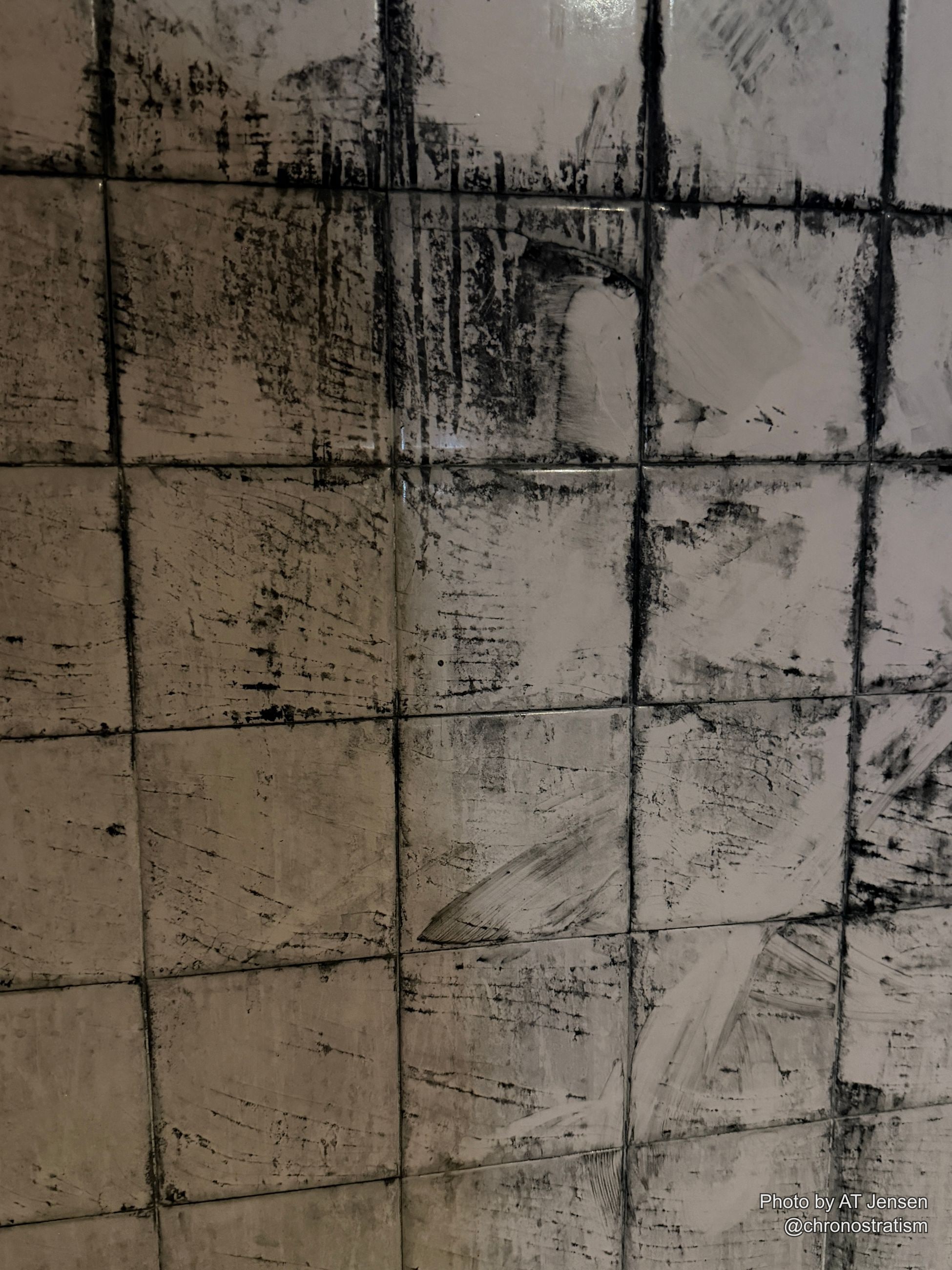 Black soot mottles a cracked ceramic tile grid in dense, uneven patches.
