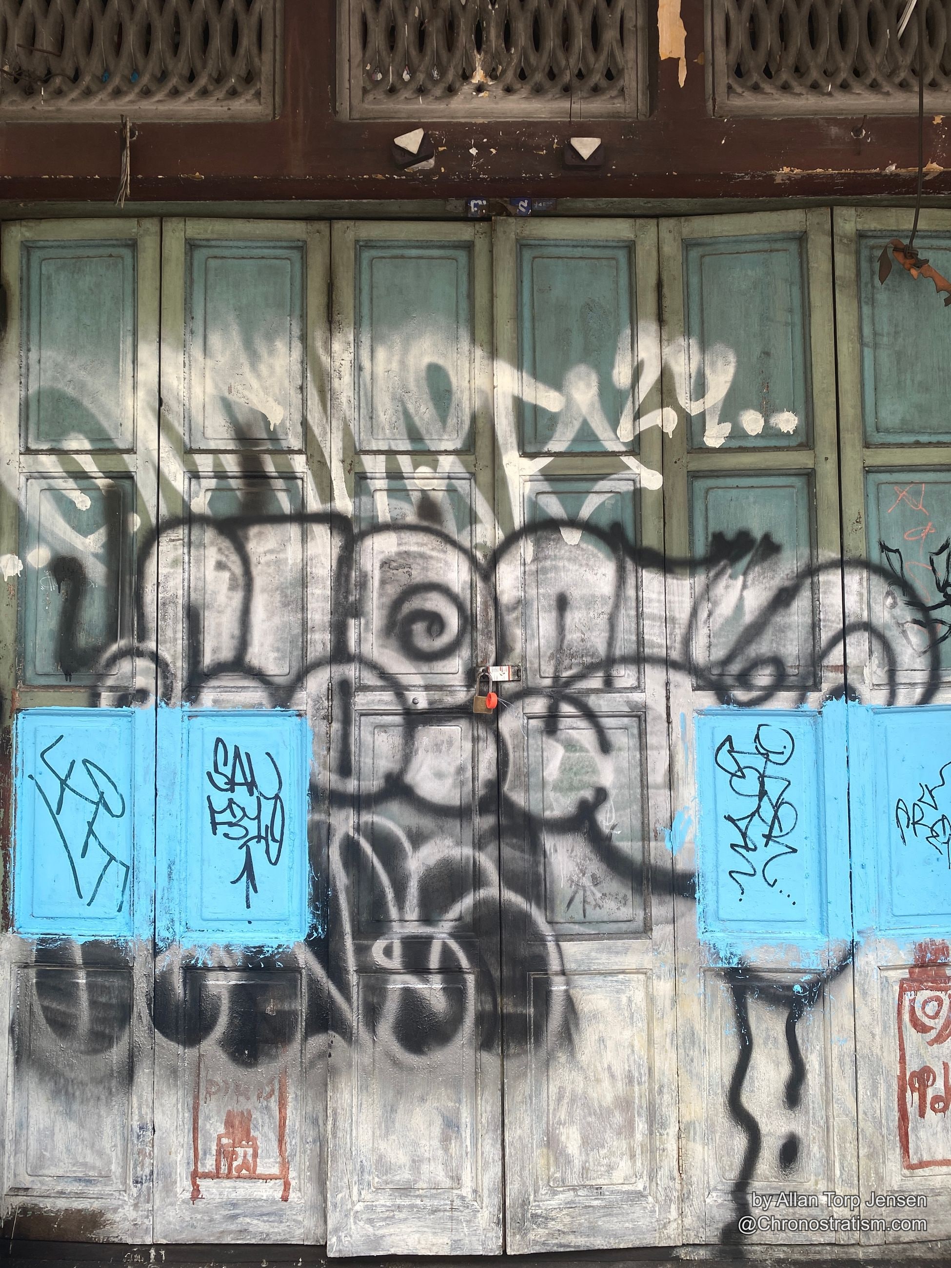 Black spray-painted tags cover ornate carved wooden door panels.