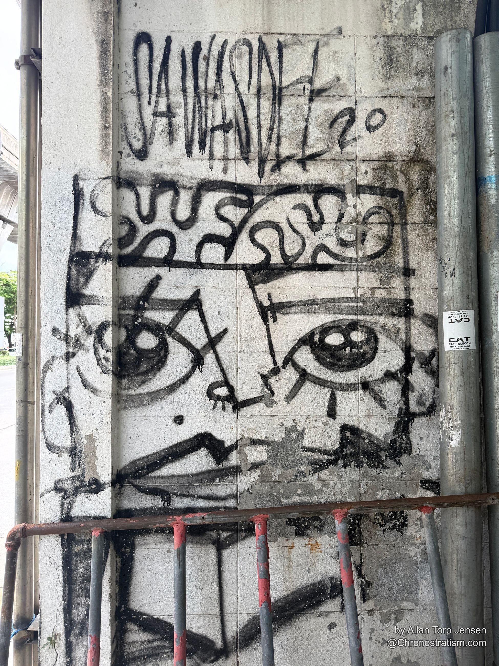 Black spray-painted tags scrawl across a pale concrete underpass panel, a fibre-optic sticker nearby.