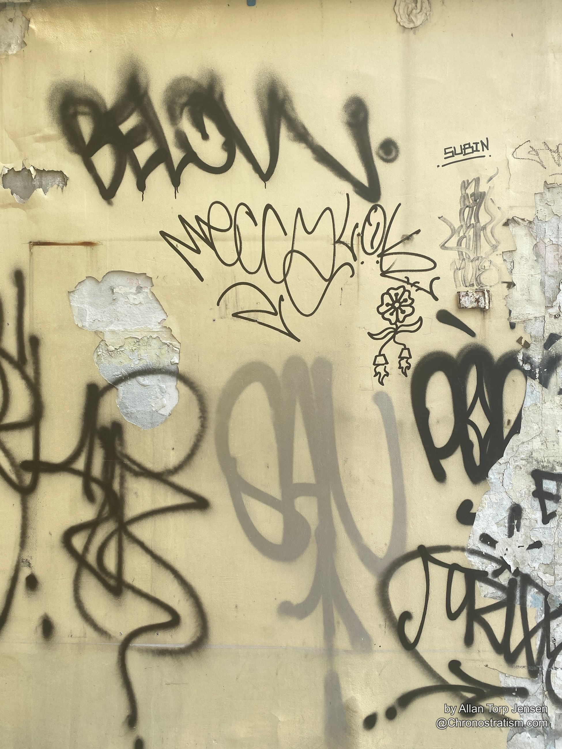 Black spray-painted tags and scrawled signatures cover a cream-painted wall.
