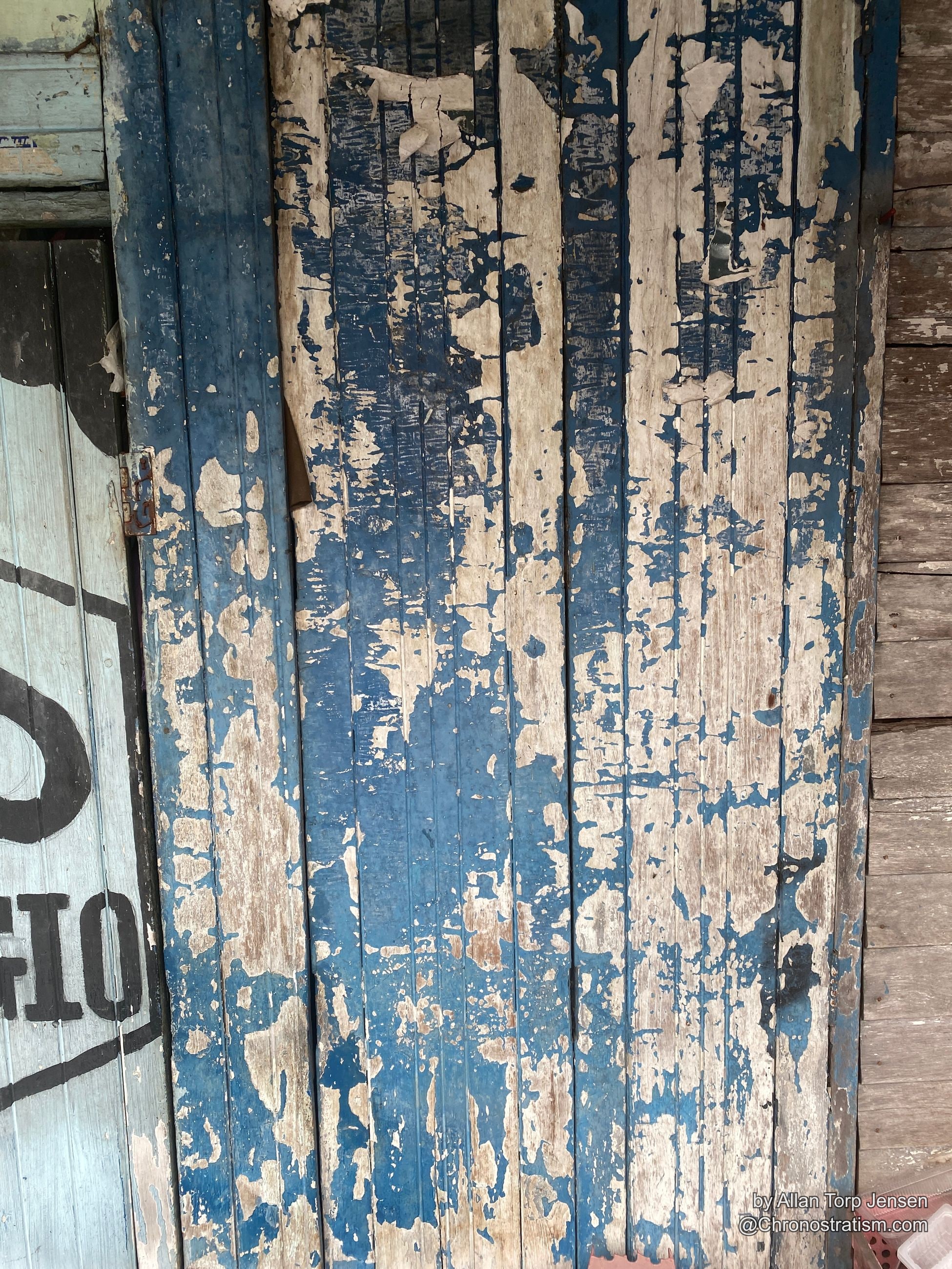 Blue and white paint peels dramatically from wooden shophouse shutters stencilled PIAGGIO.