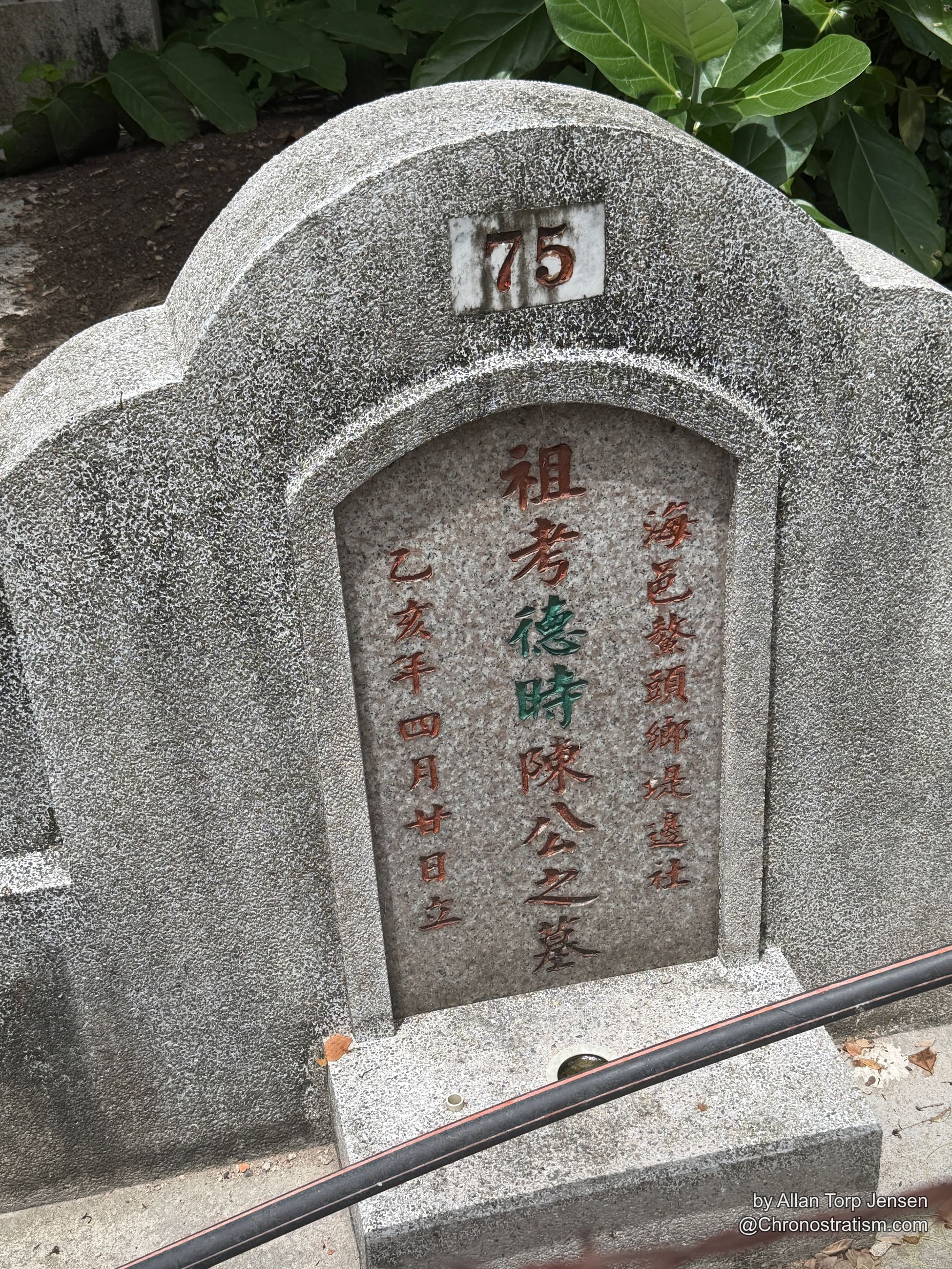 A carved stone memorial plaque bears red and green painted characters beside scattered leaves.