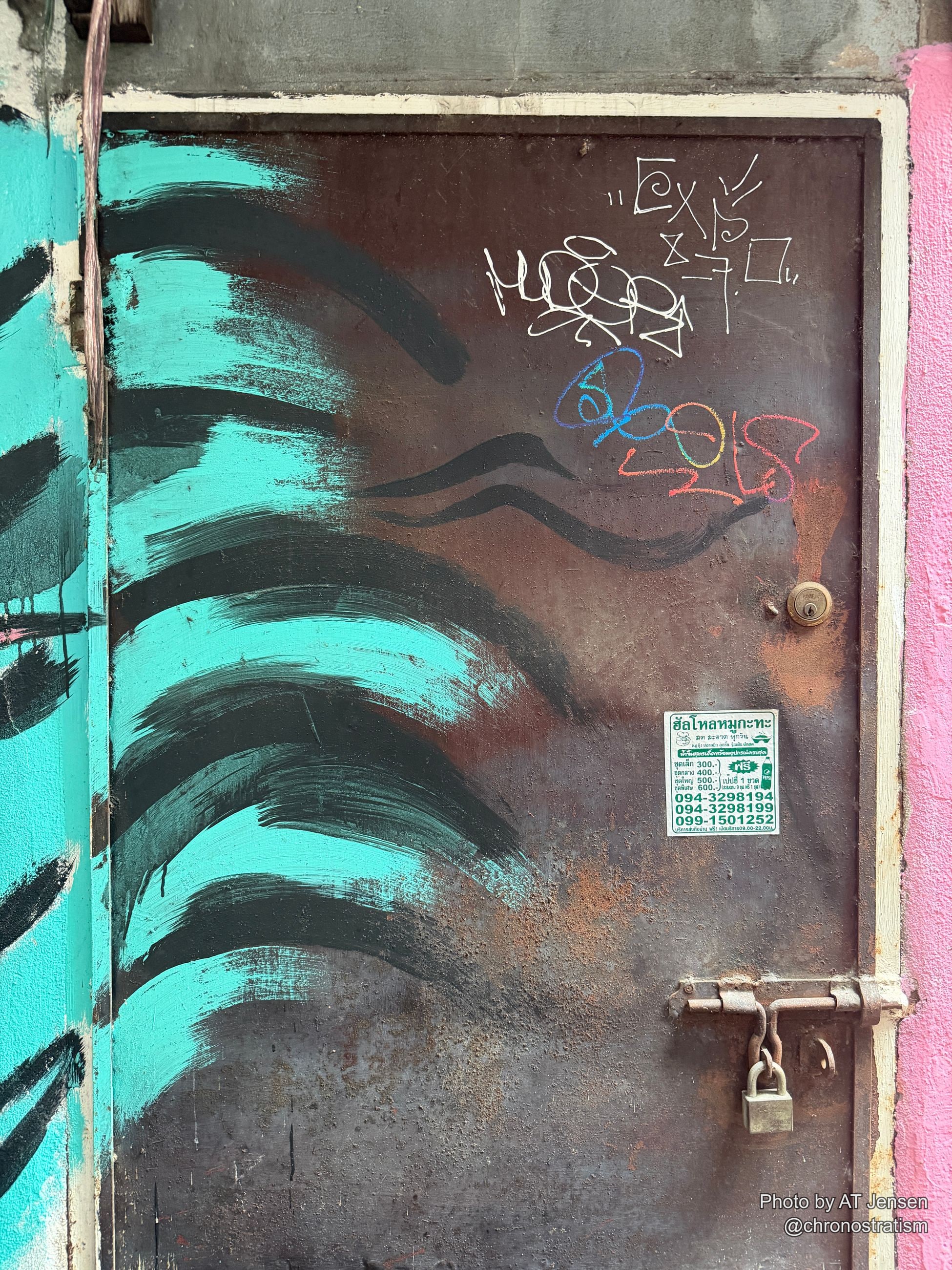 Colourful chalk graffiti and teal brush strokes cover a rusted metal door bolted with a padlock.