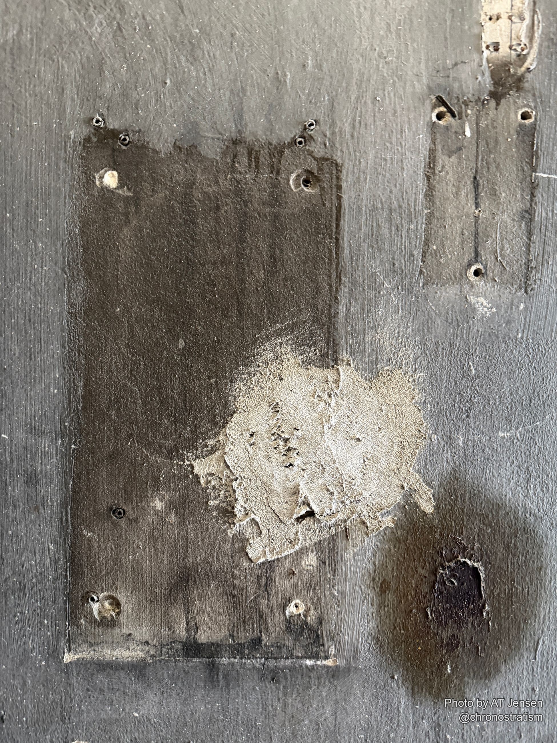 A charred, soot-blackened scorch mark spreads across a grey-painted panel patched with an old cement repair.