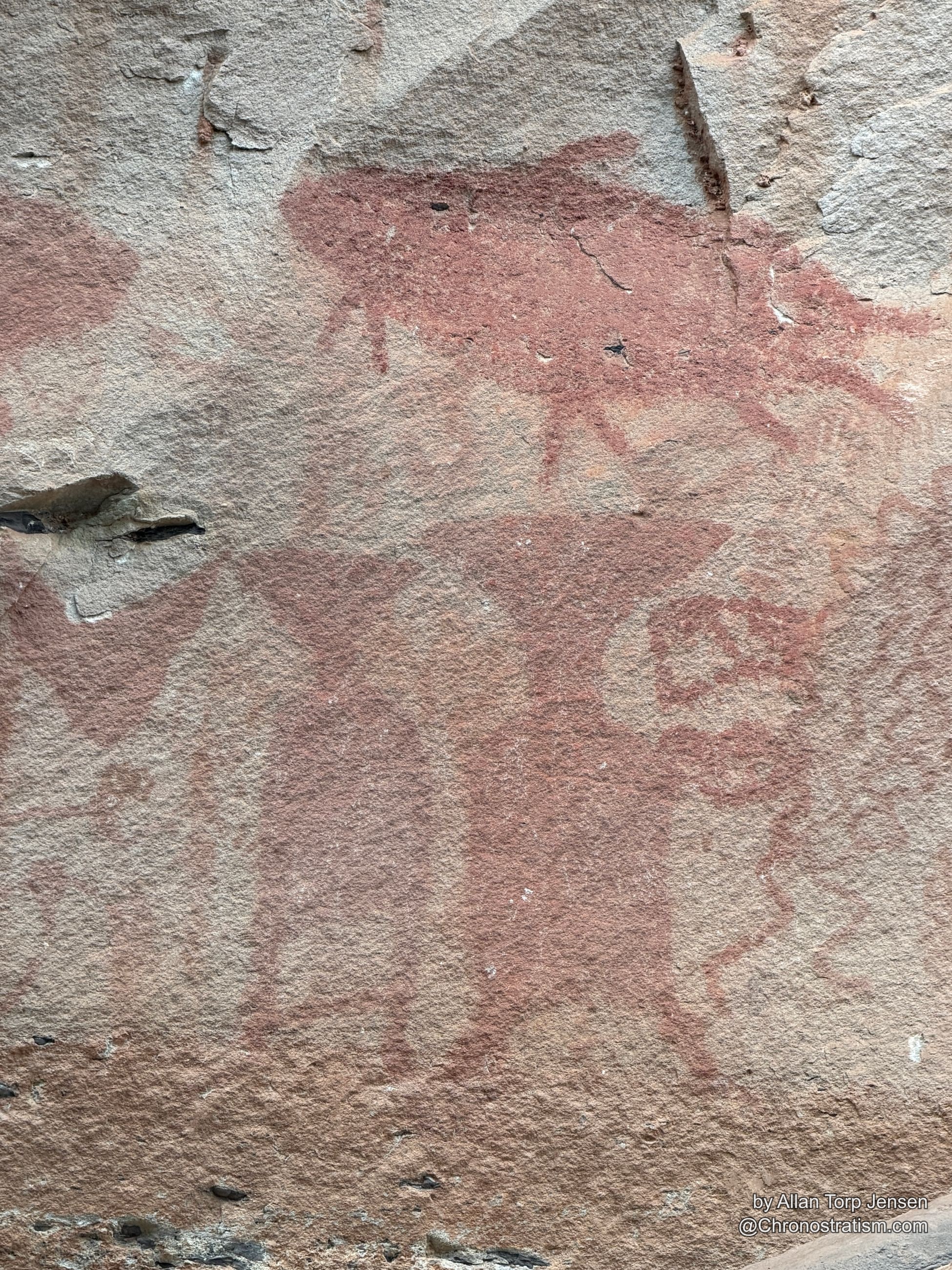Closer view of the ochre pictograph symbol bleeding into the stone’s weathered surface.