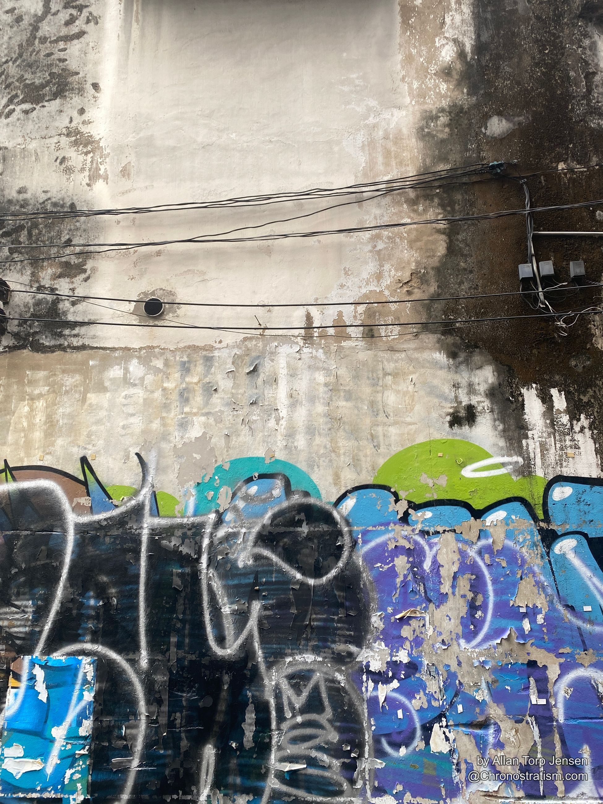 Colorful mural characters emerge from a soot-stained wall tangled with overhead wires.