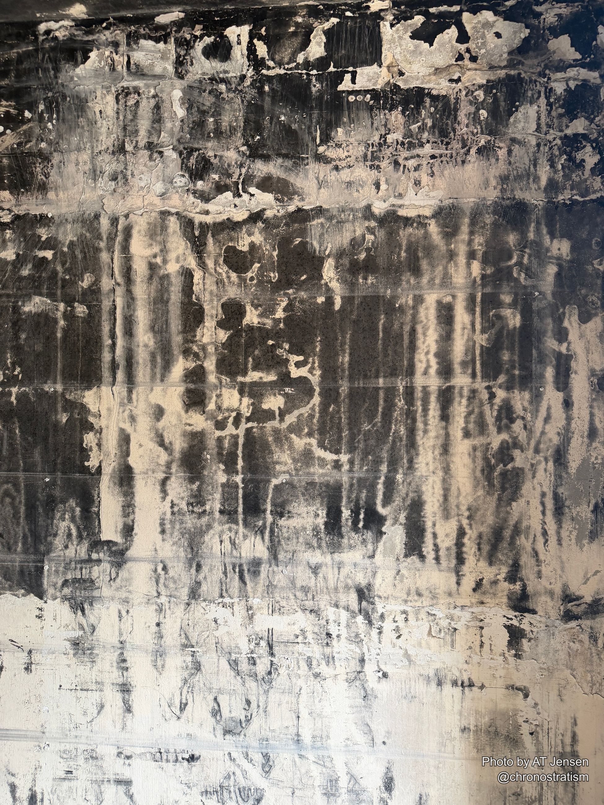 Dark soot streaks cascade down a cream-painted wall in dramatic vertical stripes.