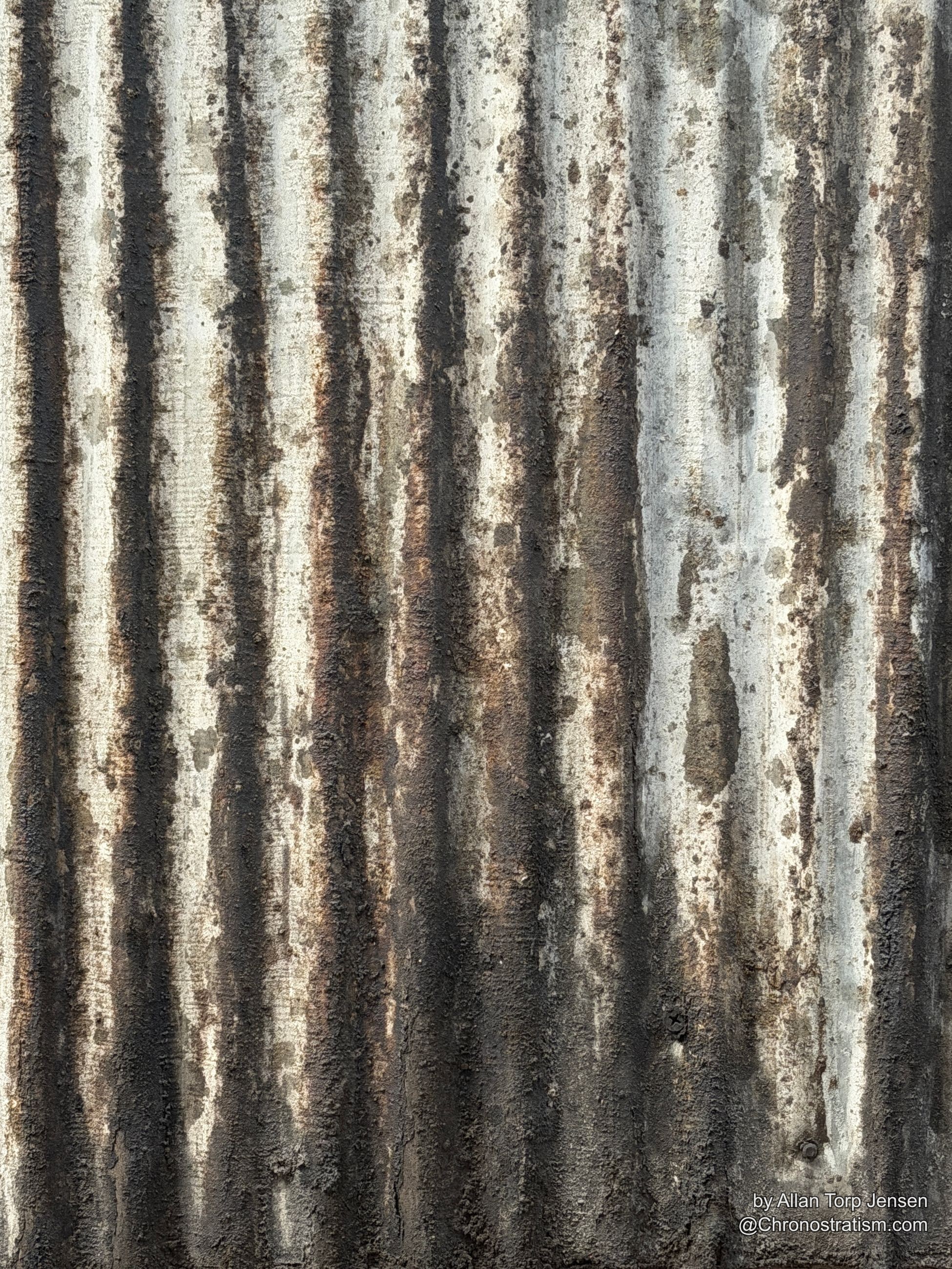 Dark soot streaks cascade down a corrugated metal fence in dense vertical stripes.