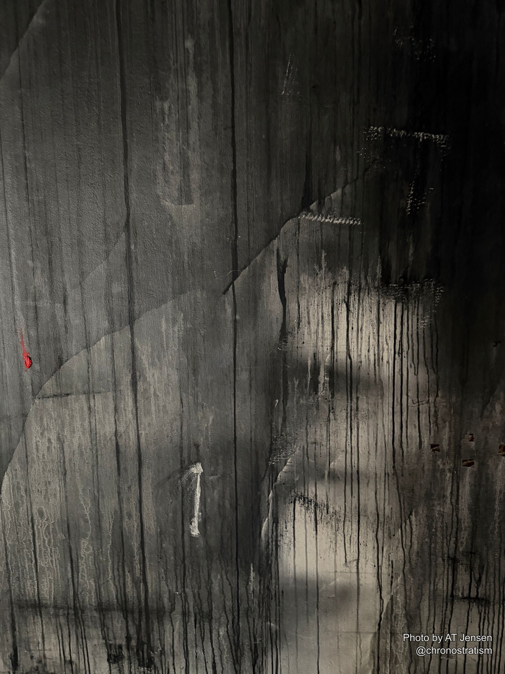 Dark soot streaks bleed down weathered concrete, a faded red mark surviving faintly beneath.