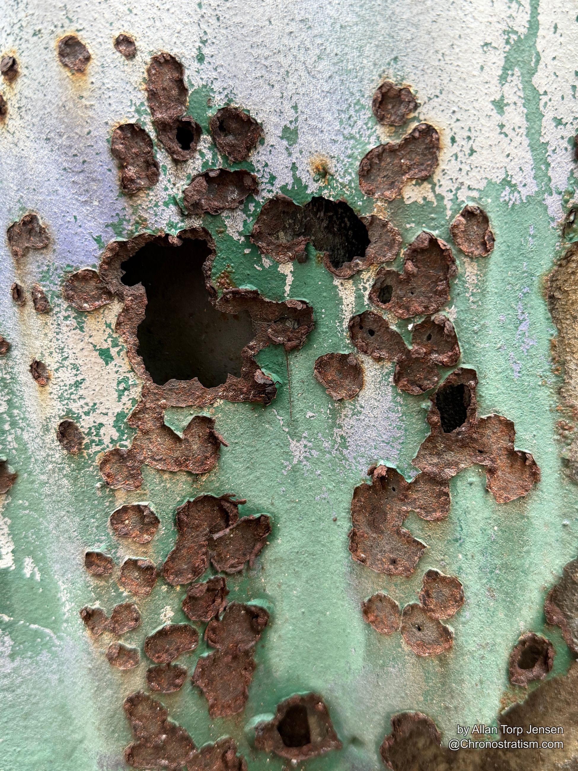 Dense rust perforates a sheet of green and white painted metal, eating clean through.