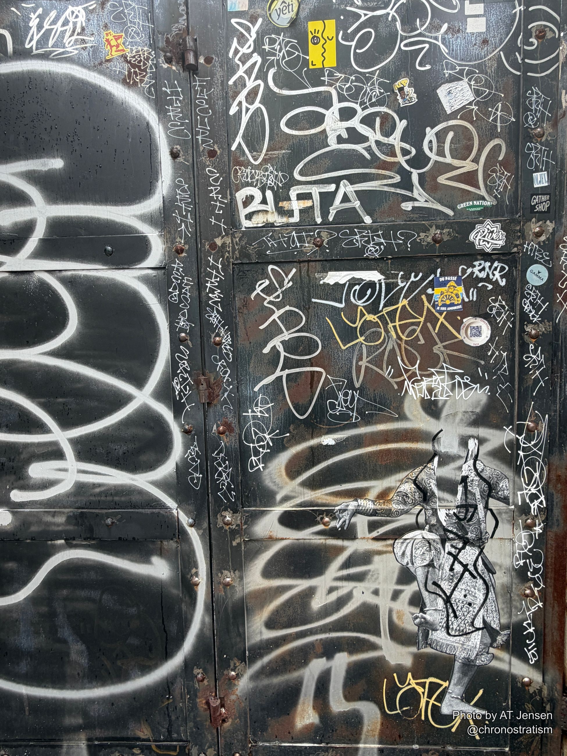 The same sticker-covered surface continues past a monochrome paste-up figure tangled in spray-paint loops.
