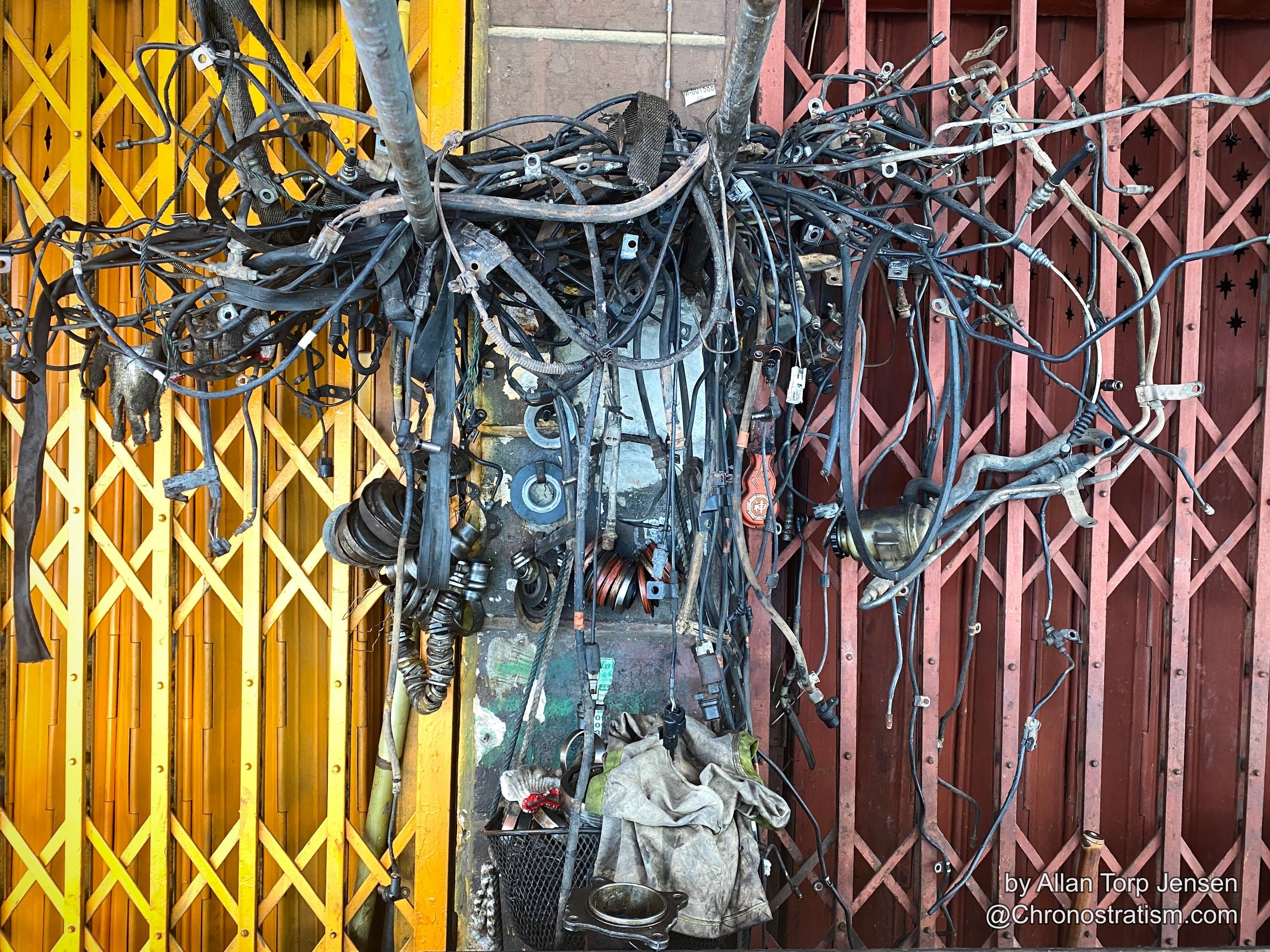 A dense tangle of automotive wiring harnesses hangs like a nest on a market shutter.