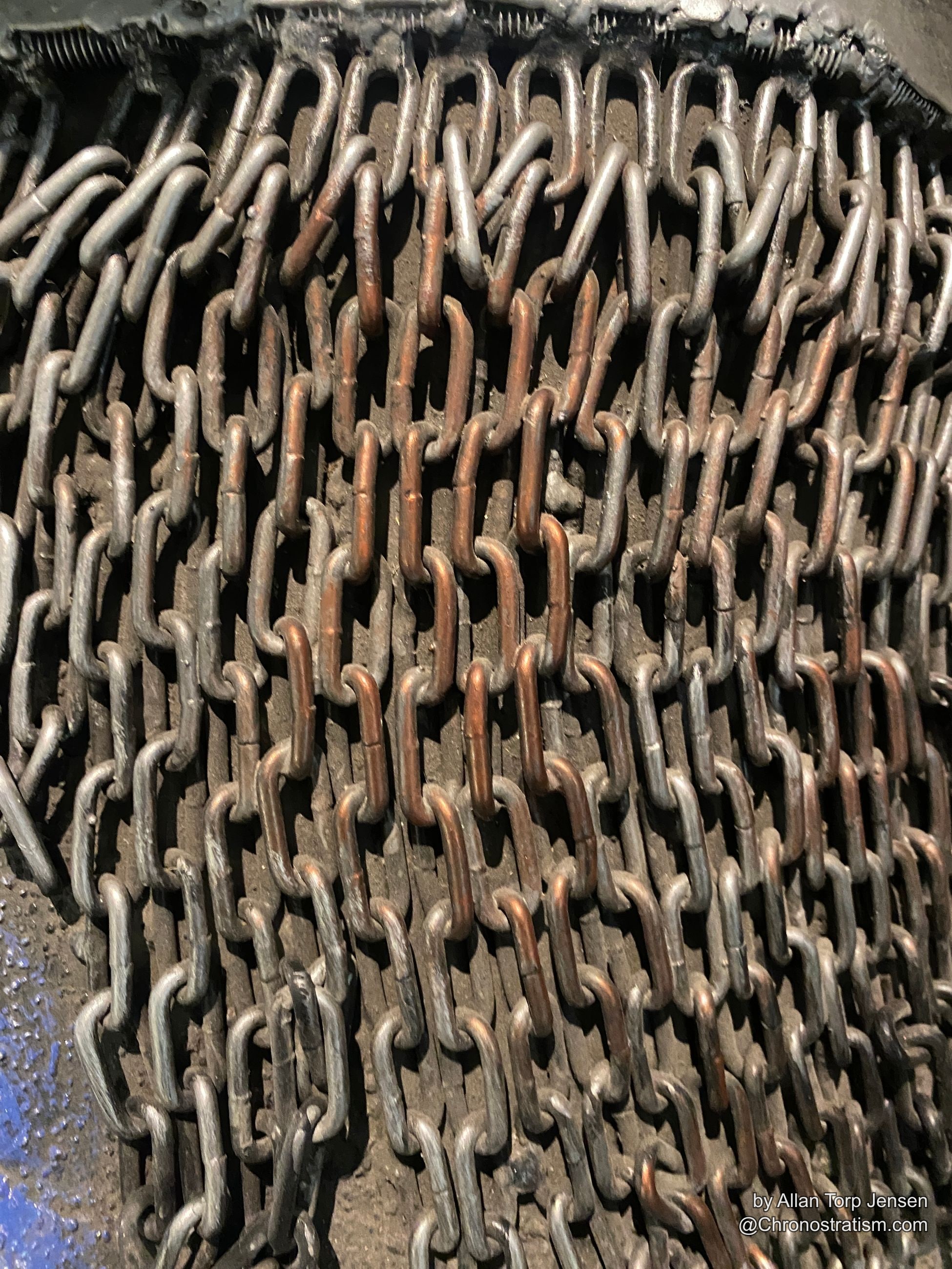 A dense woven curtain of rusted steel chain links, copper-toned oxidation at every joint.