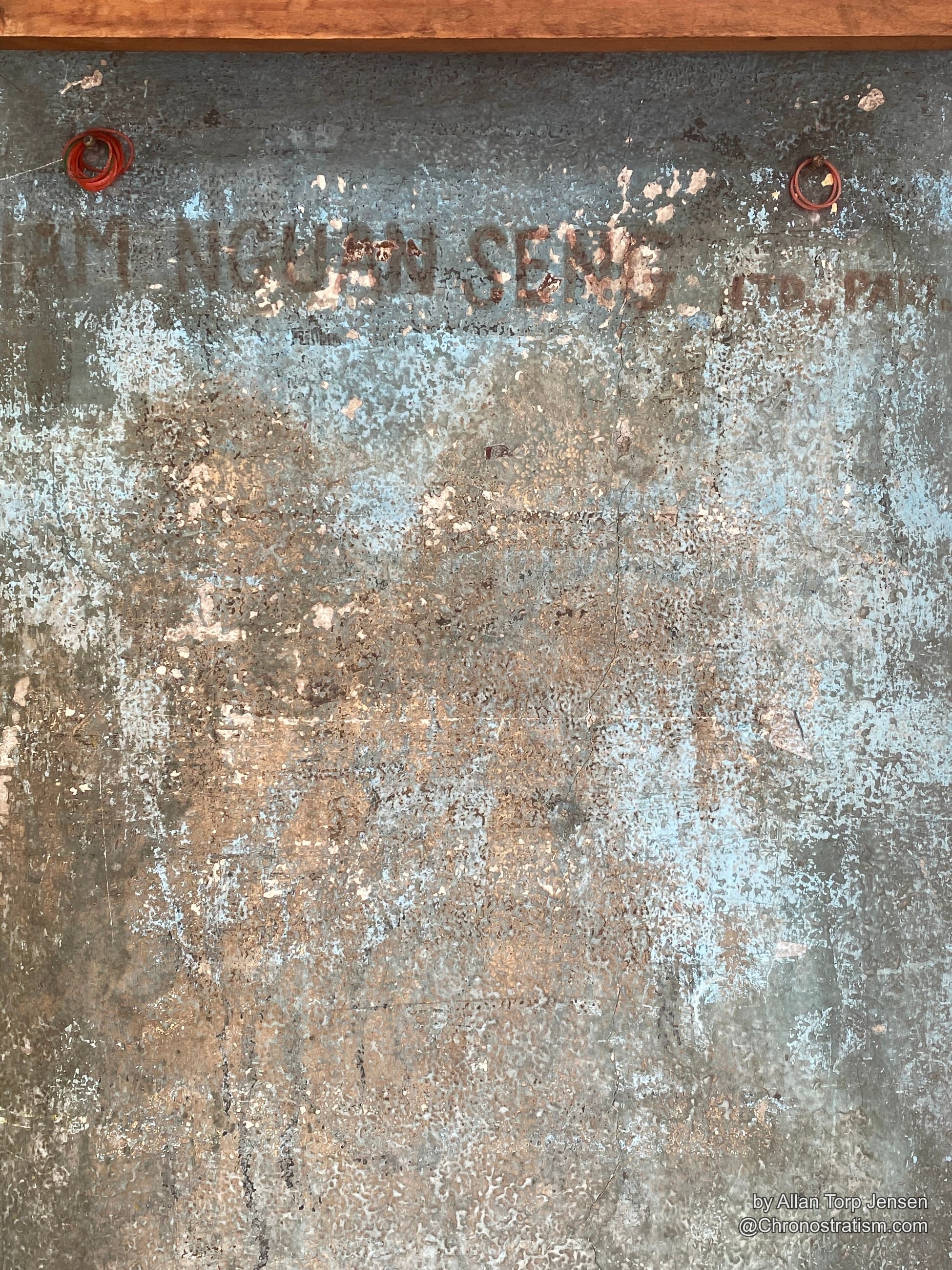 A faded ghost-sign advertisement clings to a weathered galvanized metal panel.