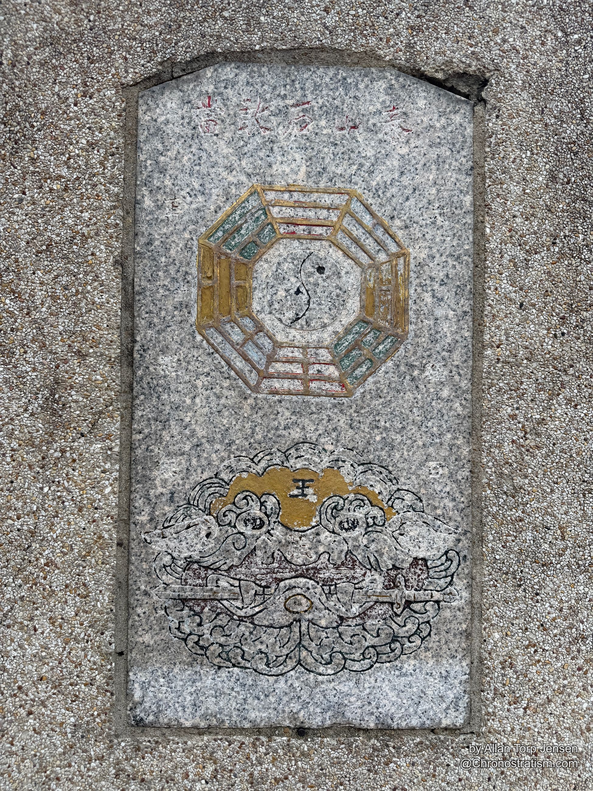 A gilded bagua mirror and carved guardian figure are inlaid into a granite pavement slab.