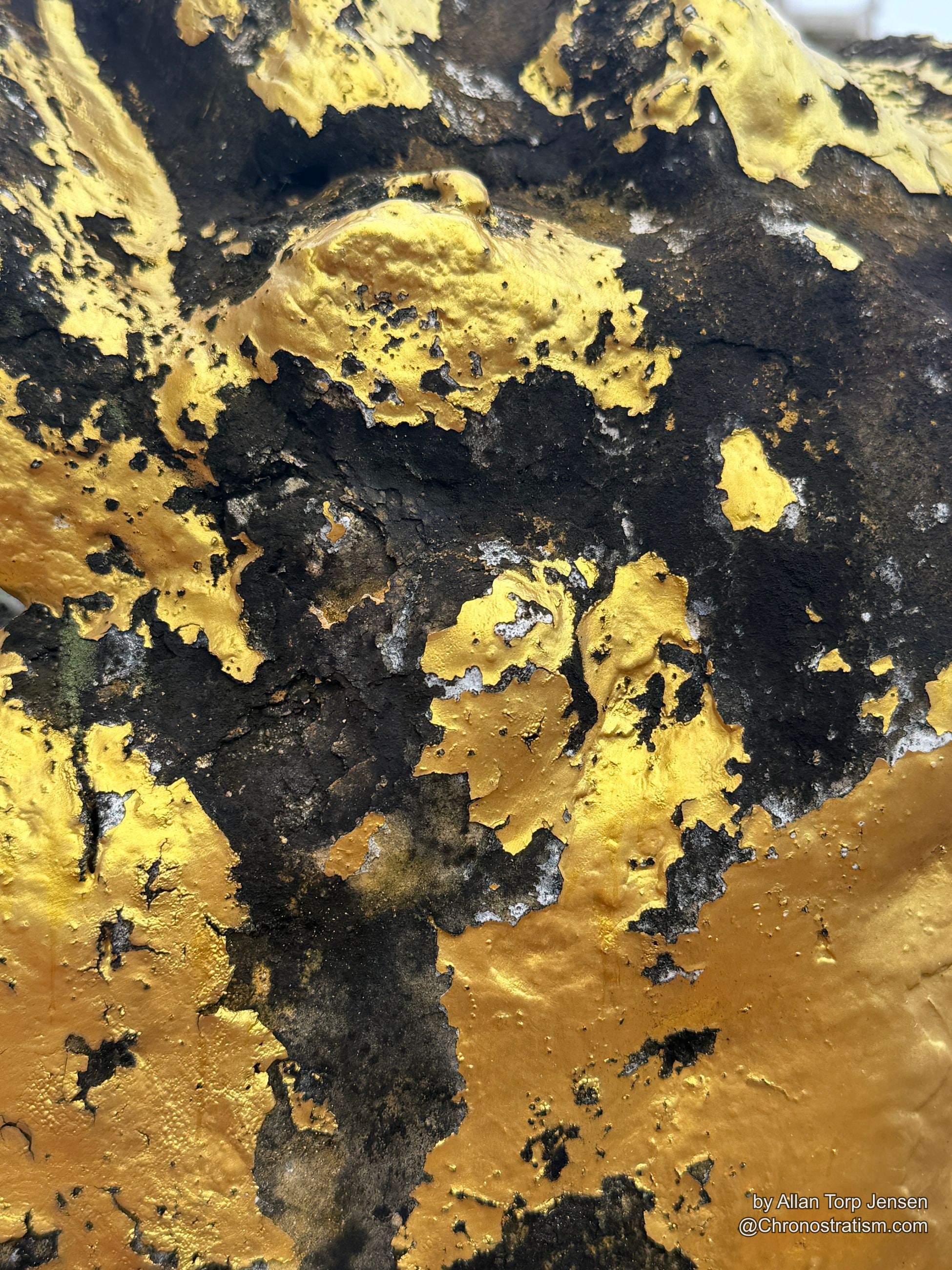 Gold leaf clings in irregular islands across a heavily sooted surface.