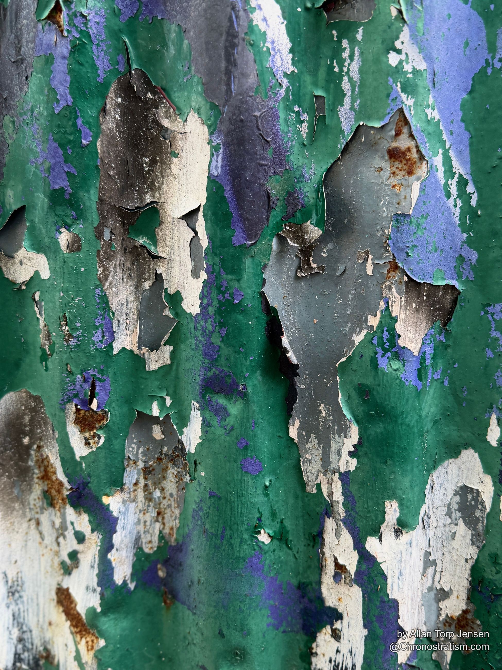 Green and purple paint peels away from a heavily rusted metal surface in jagged sheets.