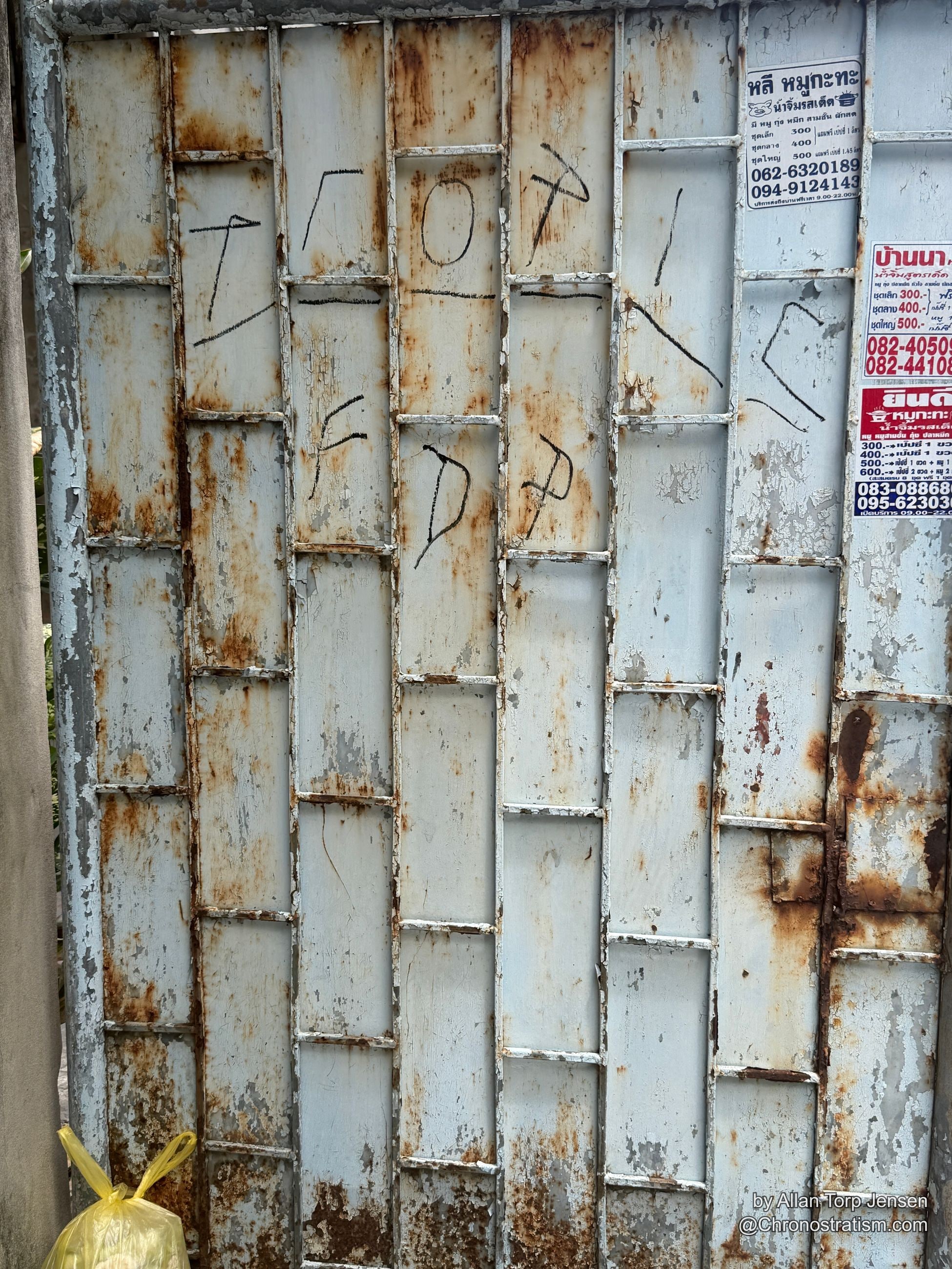 Hand-scrawled chalk doodles and business phone-number stickers cover a rusty corrugated wall.