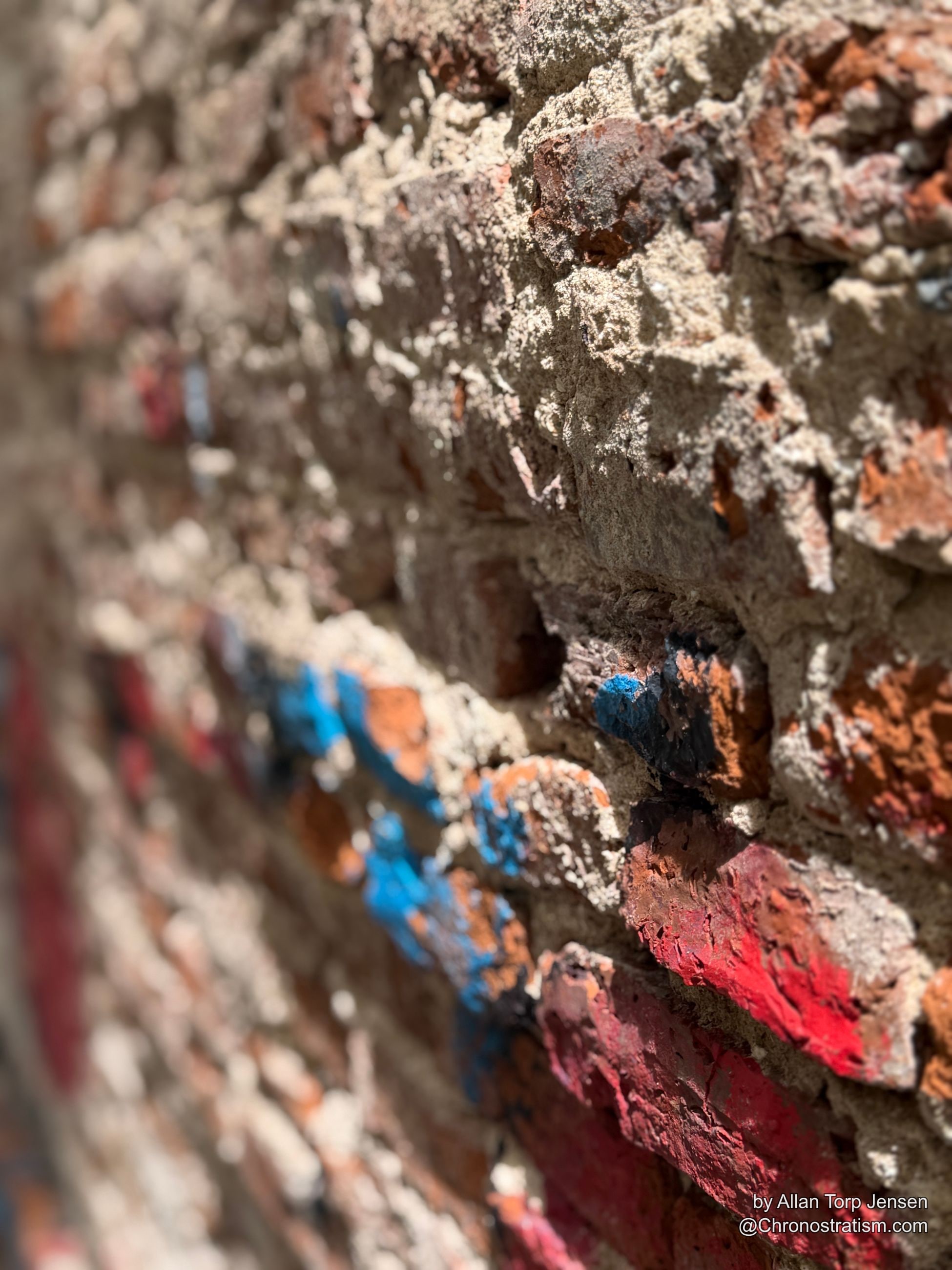 Macro detail of the red paint’s cracked, weathered surface over old brick.