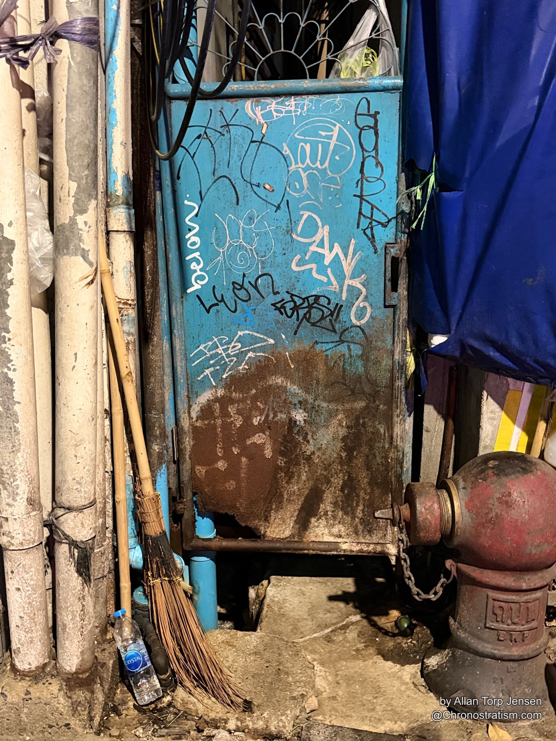 Marker graffiti tags cover a blue metal cabinet beside a rusted fire hydrant.