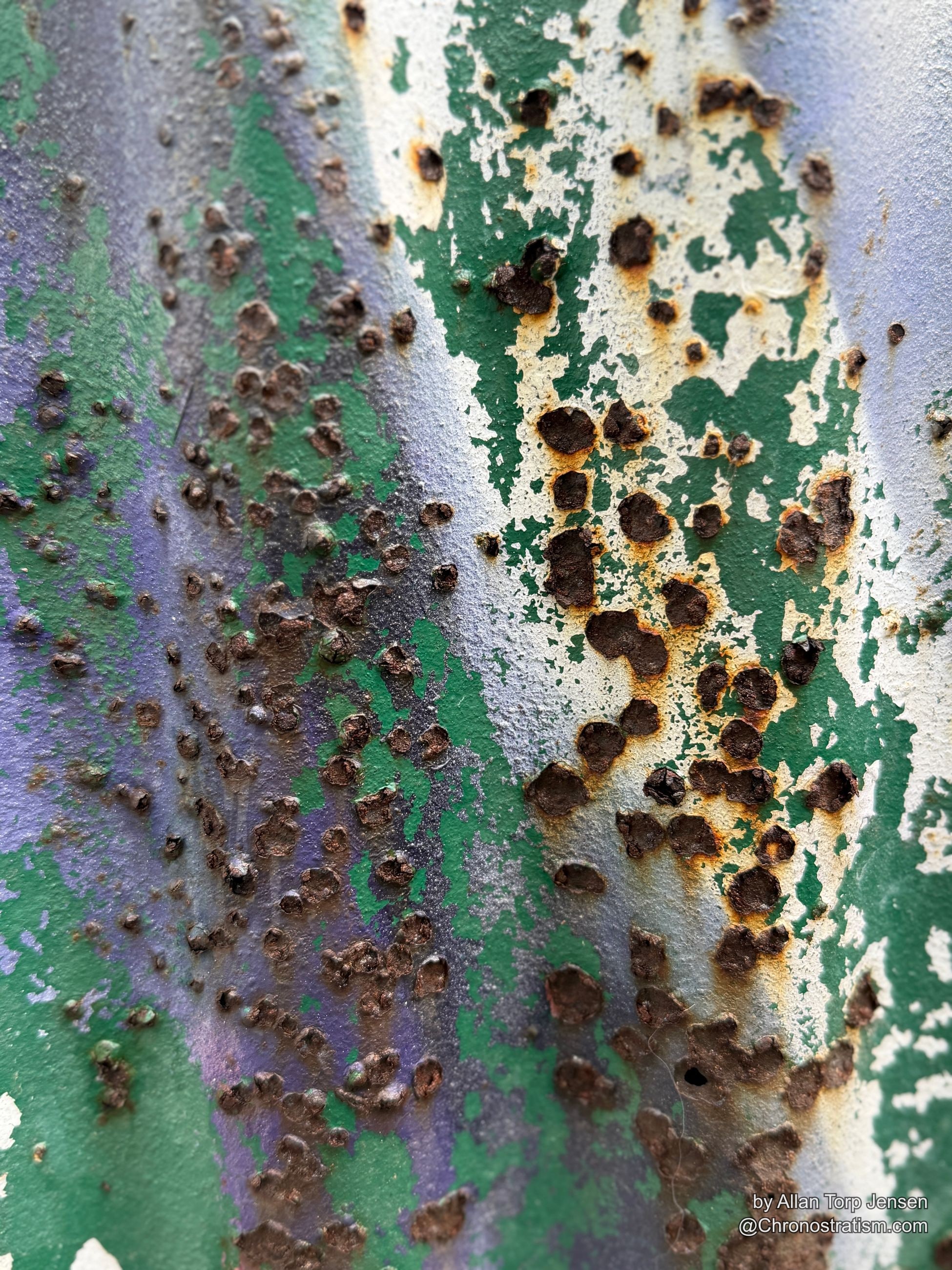 Paint peels back around a line of rivets, exposing bare metal beneath.