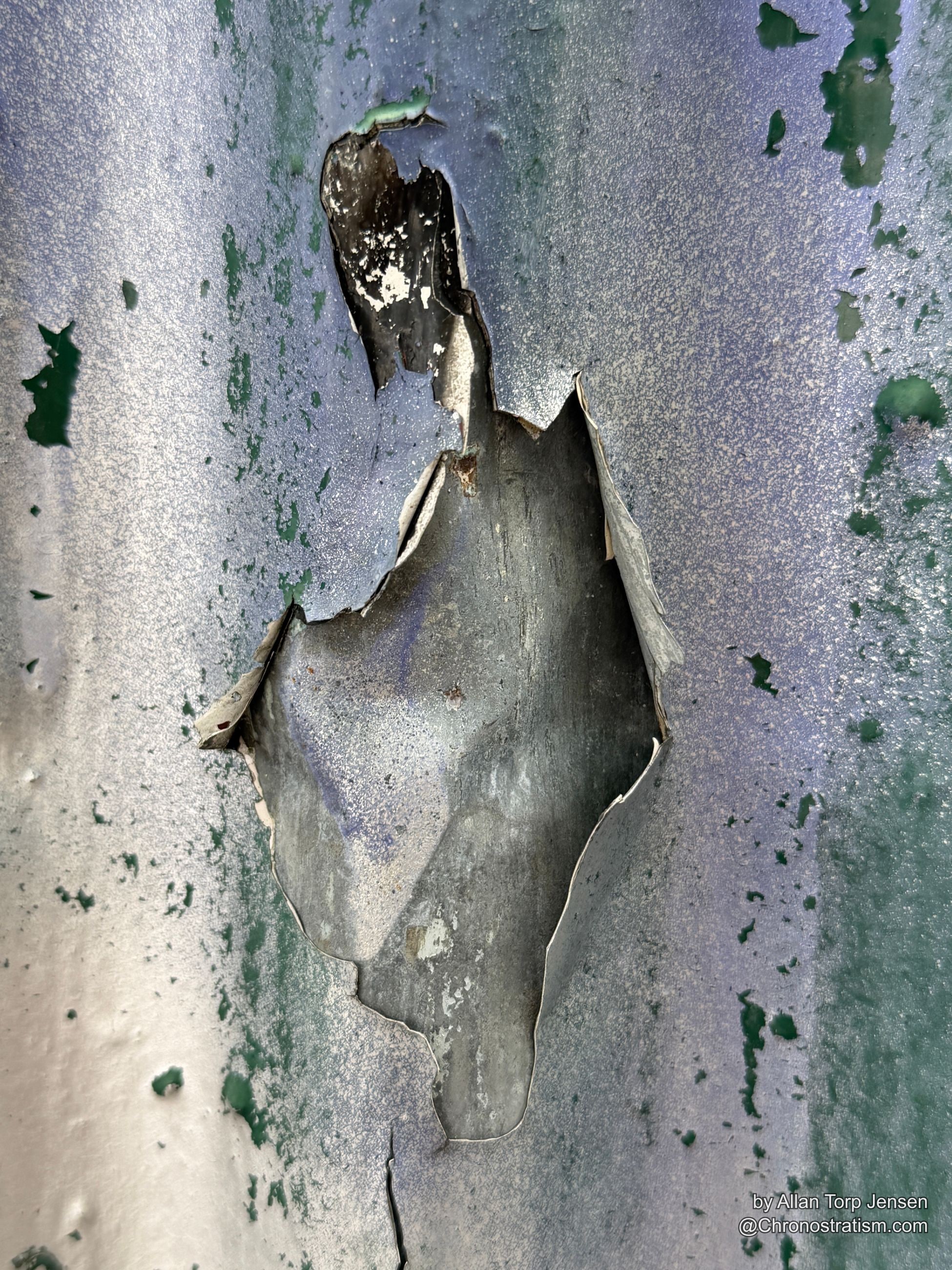 Paint tears back in a ragged sheet, forming a hole in the blue-grey surface.