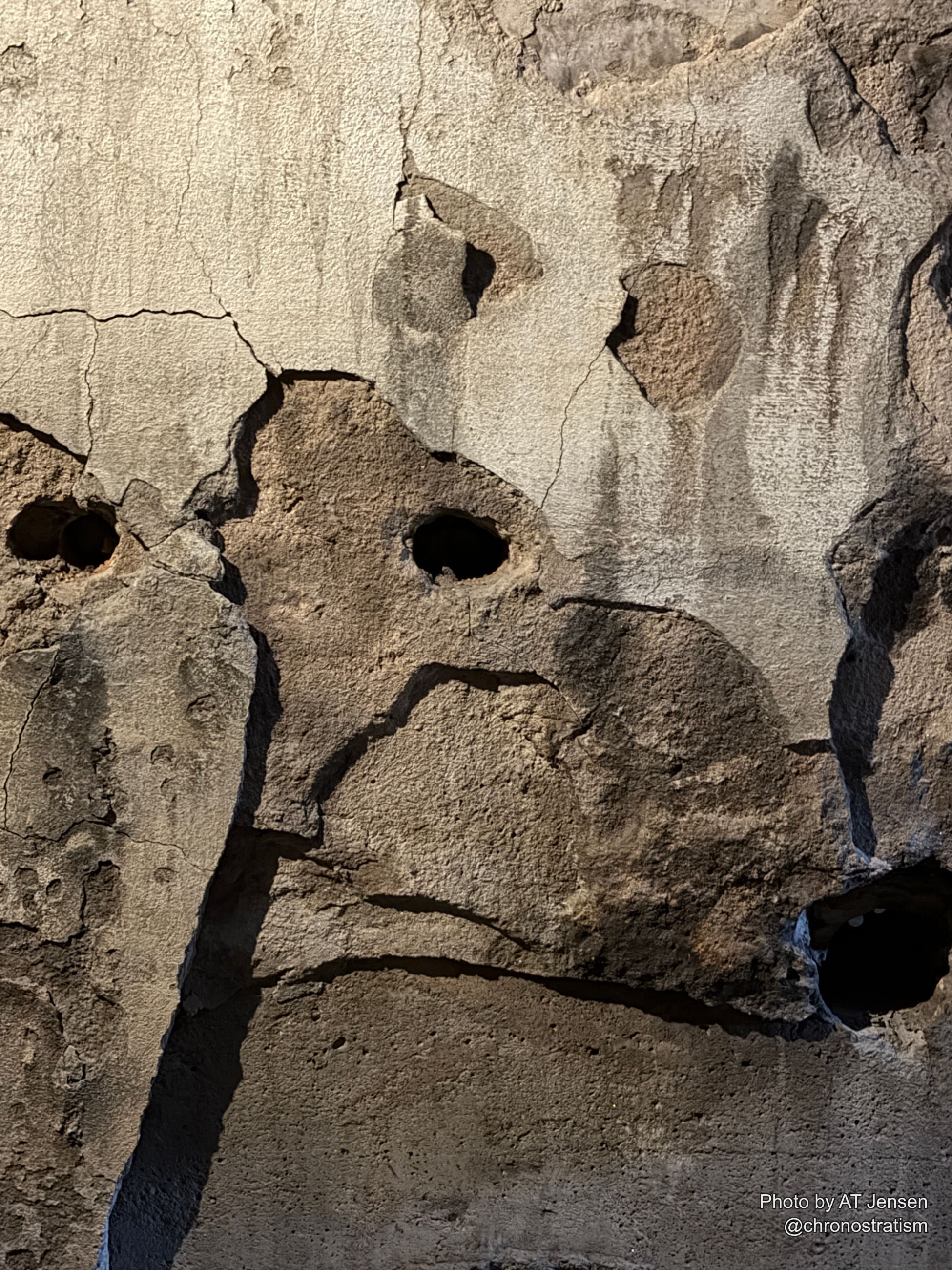 Porous, eroded stone is pocked with cratered holes and fine cracks, sunlight raking deep shadows across the surface.