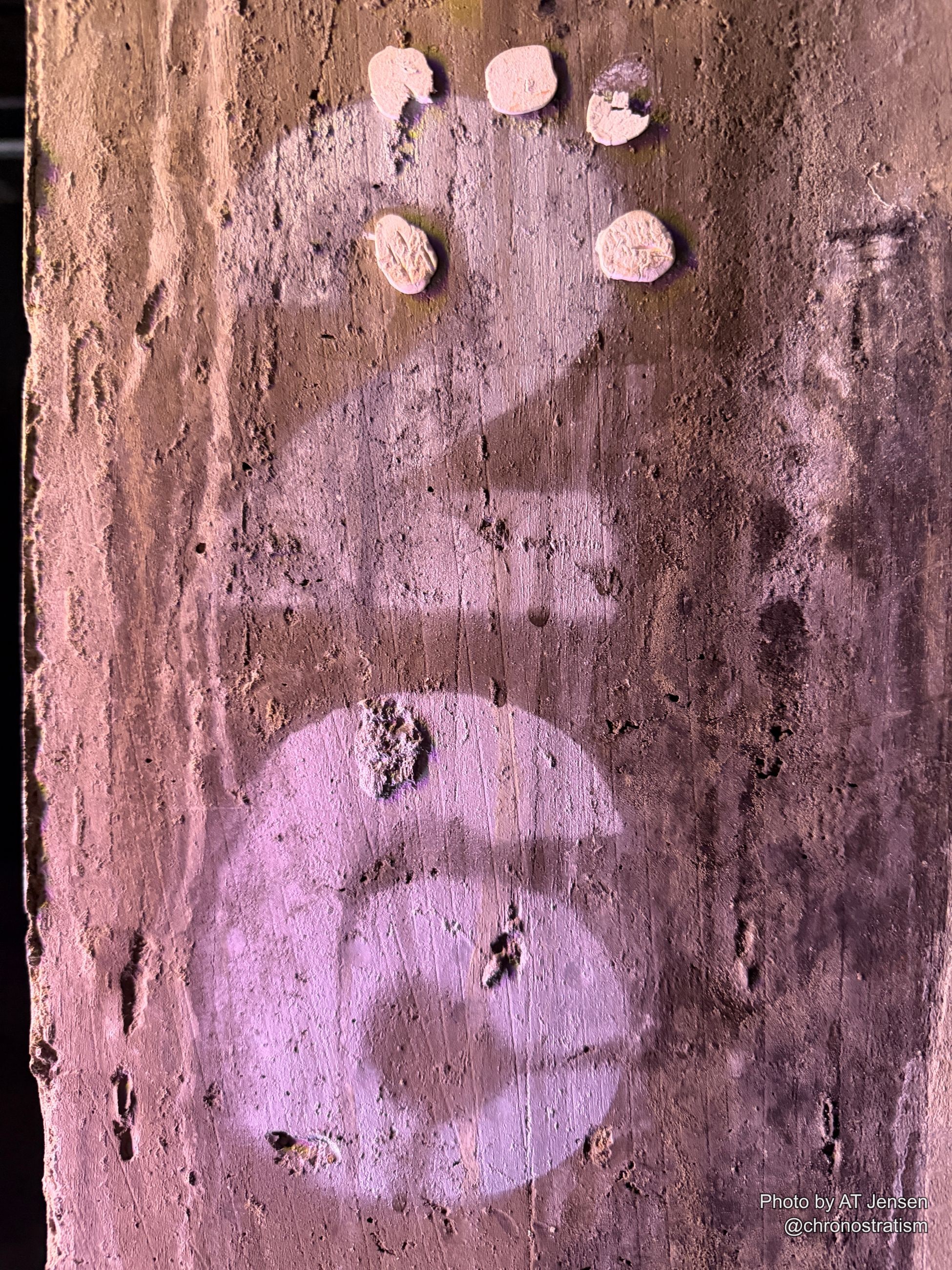 Purple stencilled lettering marks a weathered wall studded with small round ceramic adornments.