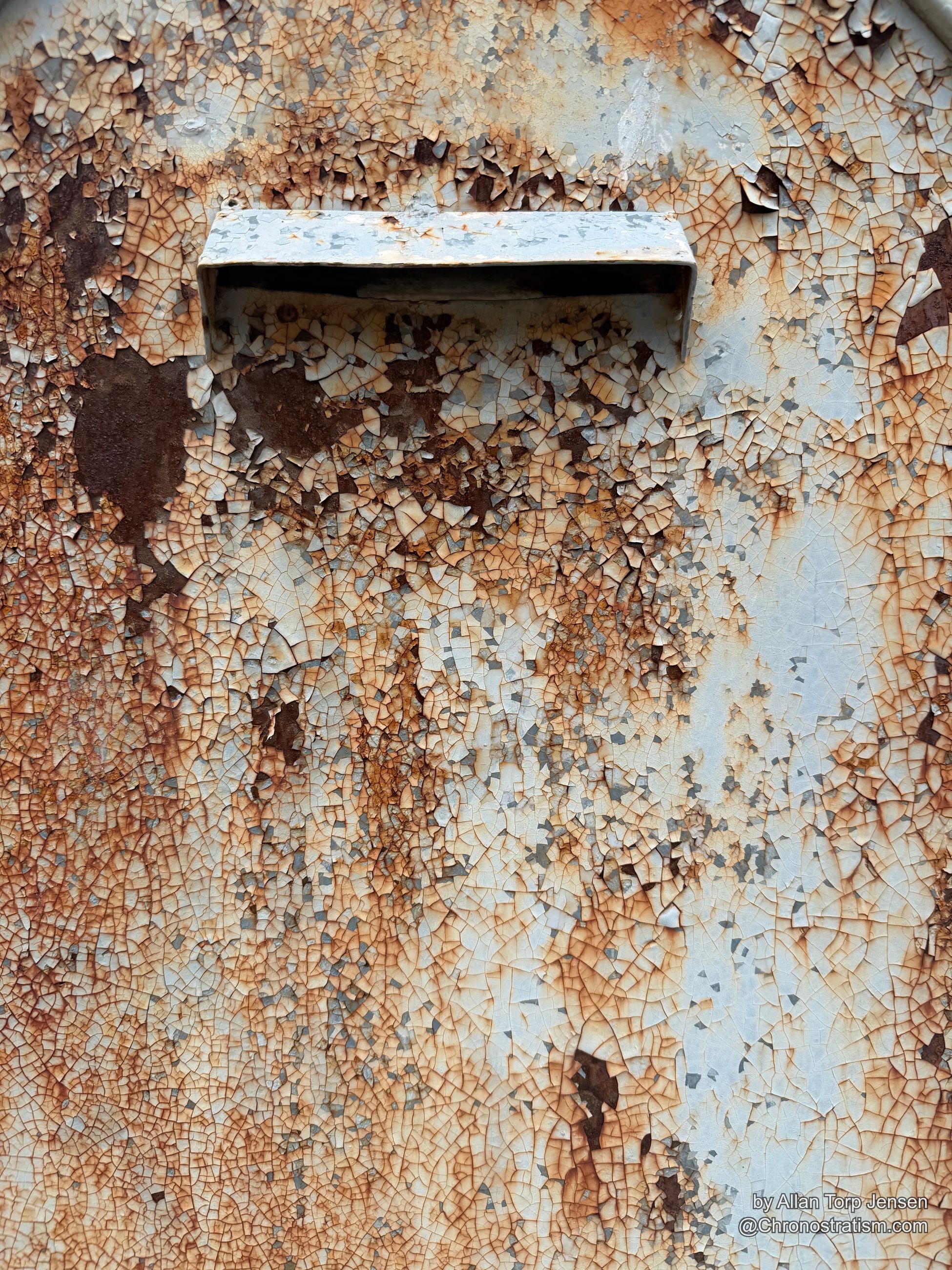 A recessed mail slot cuts into an ornate gate panel, dense craquelure webbing the surrounding cream paint.