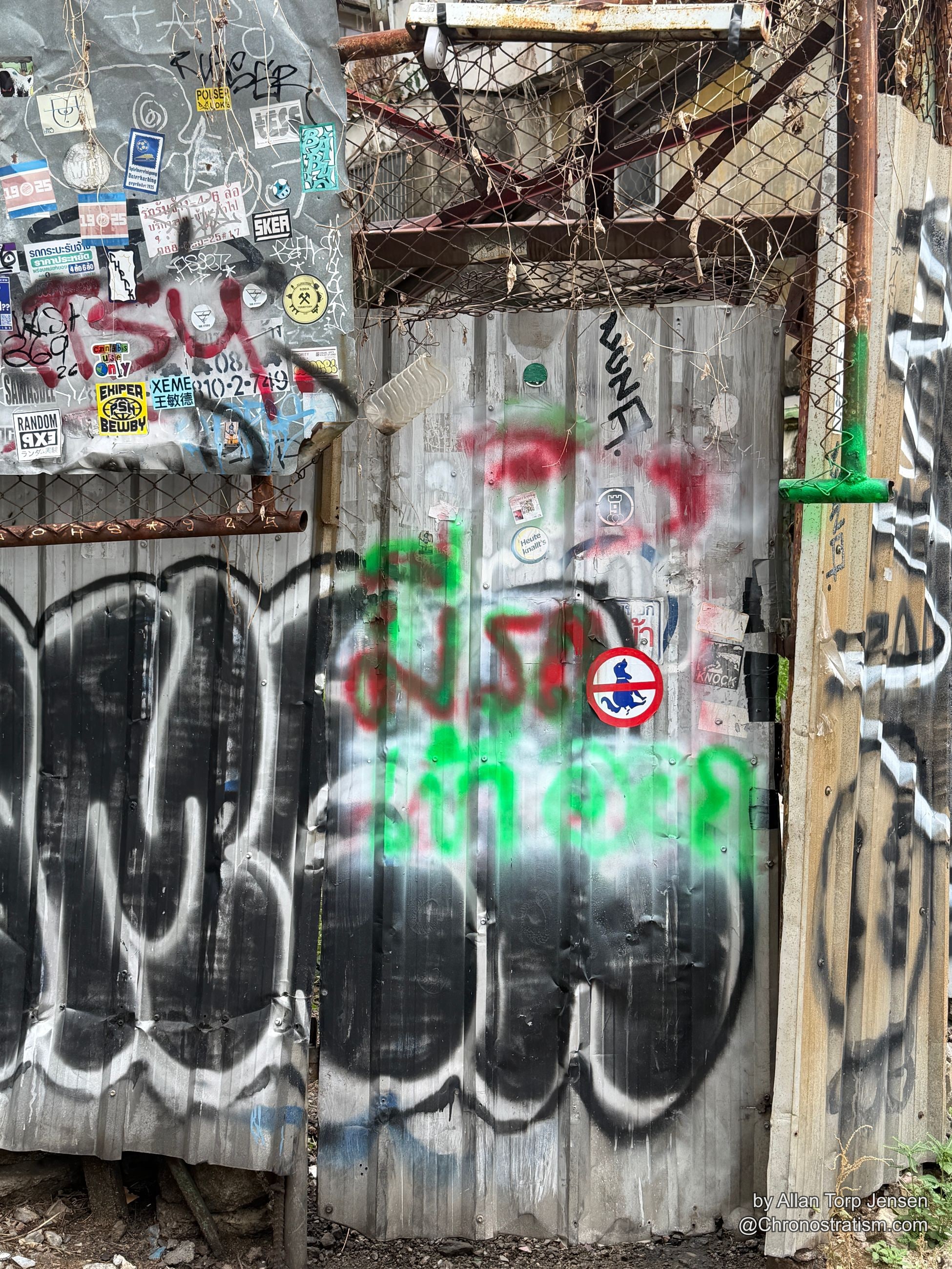 Red and green tags spread across a weathered shutter beside the sticker-covered gate.