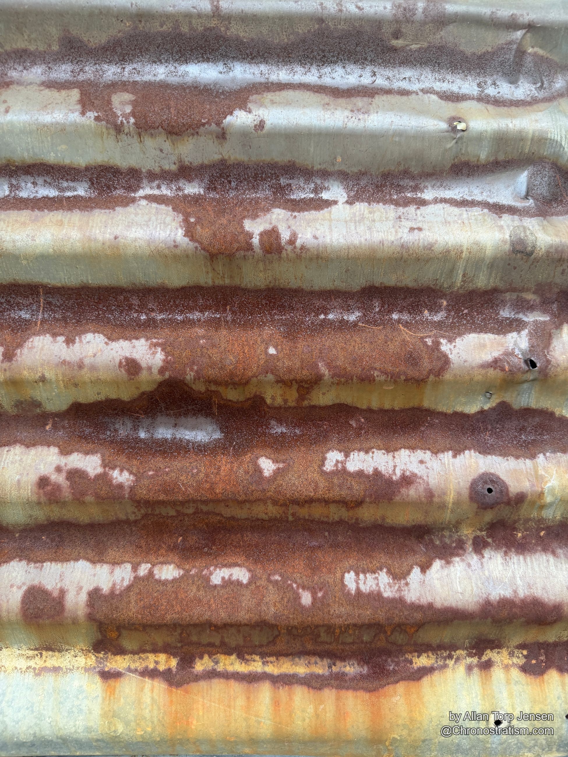Rust bleeds in dense vertical stripes down the ridges of a corrugated metal fence.
