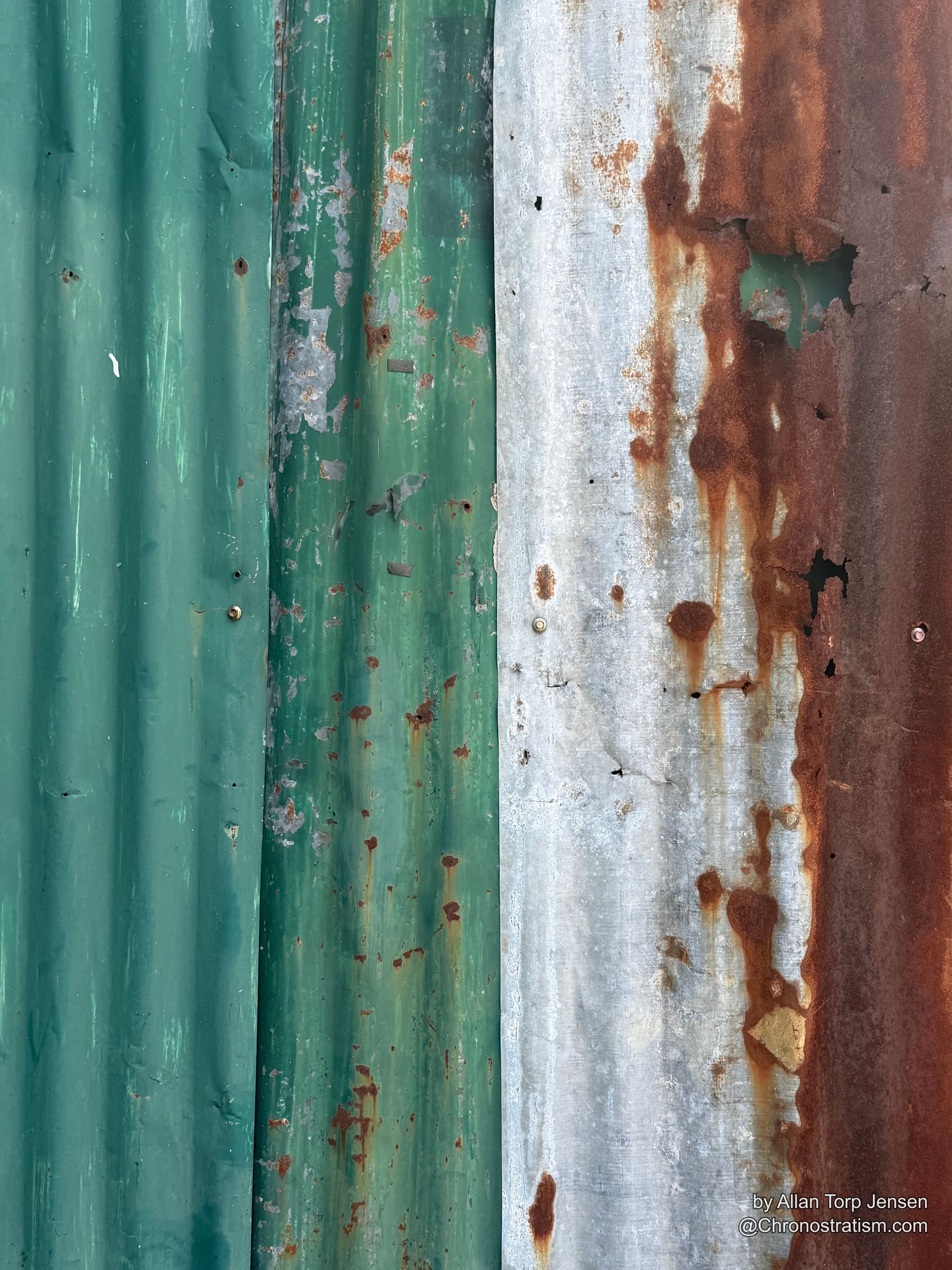 Rust bleeds through green and white corrugated fence panels in vertical streaks.