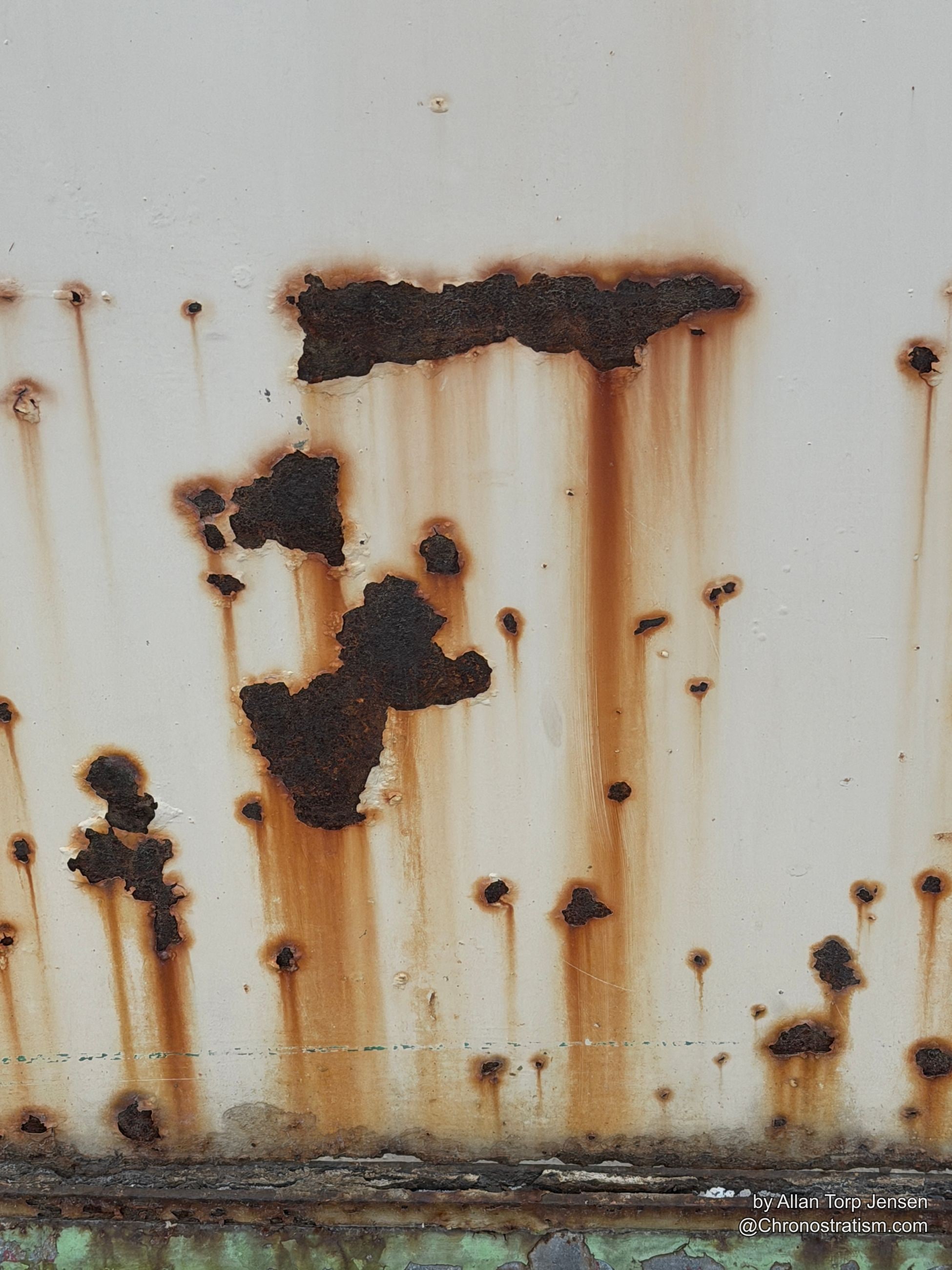 Rust bleeds in streaks down a white panel, perforating through in places.