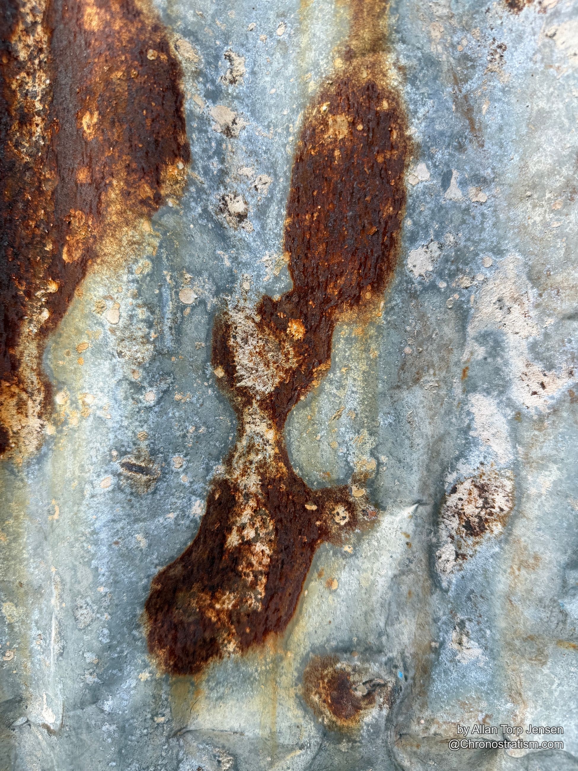 Rust patches bloom outward across a pitted galvanized surface.
