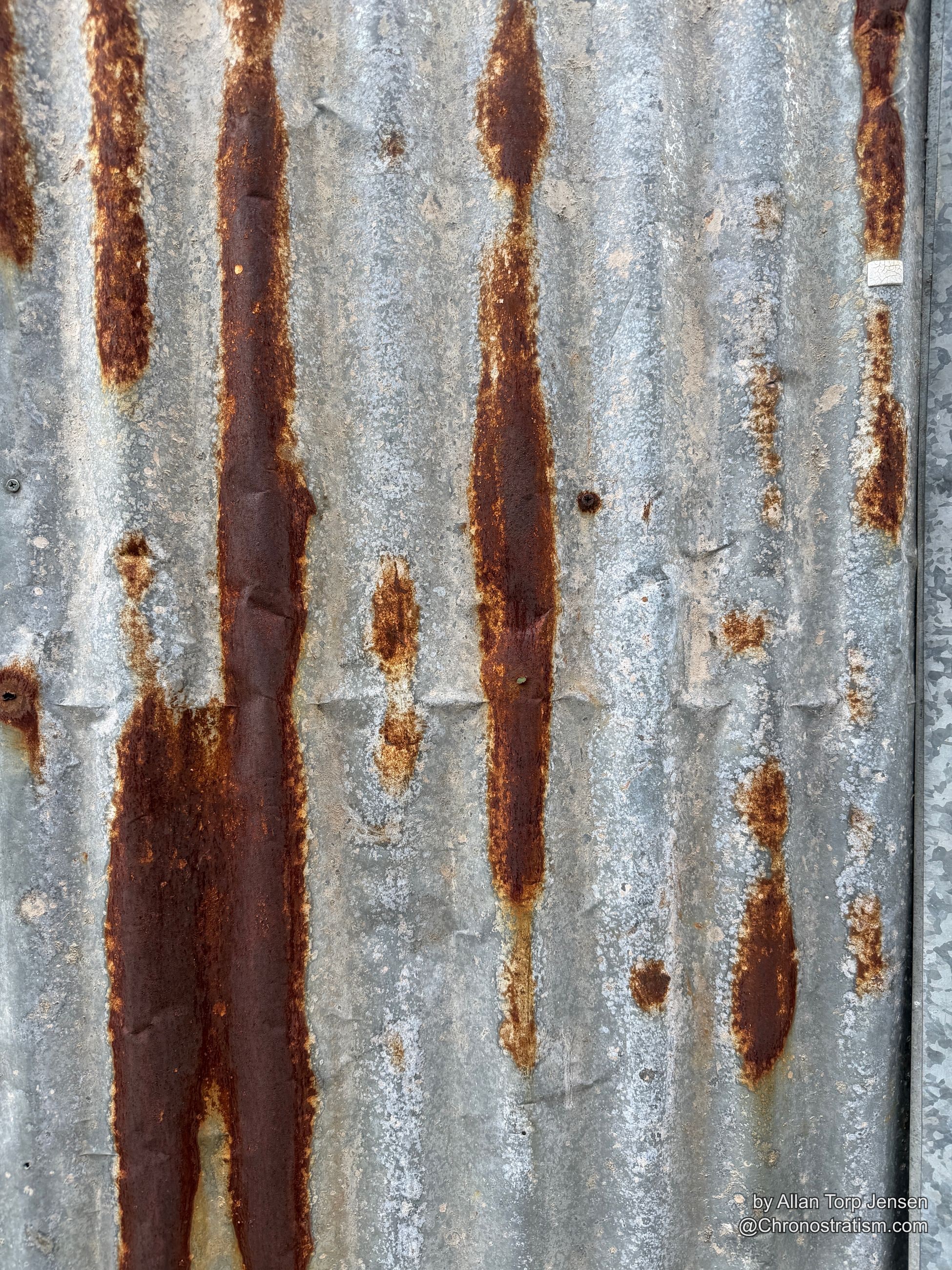 Rust patches spread across a galvanized panel beneath a torn paper sticker.