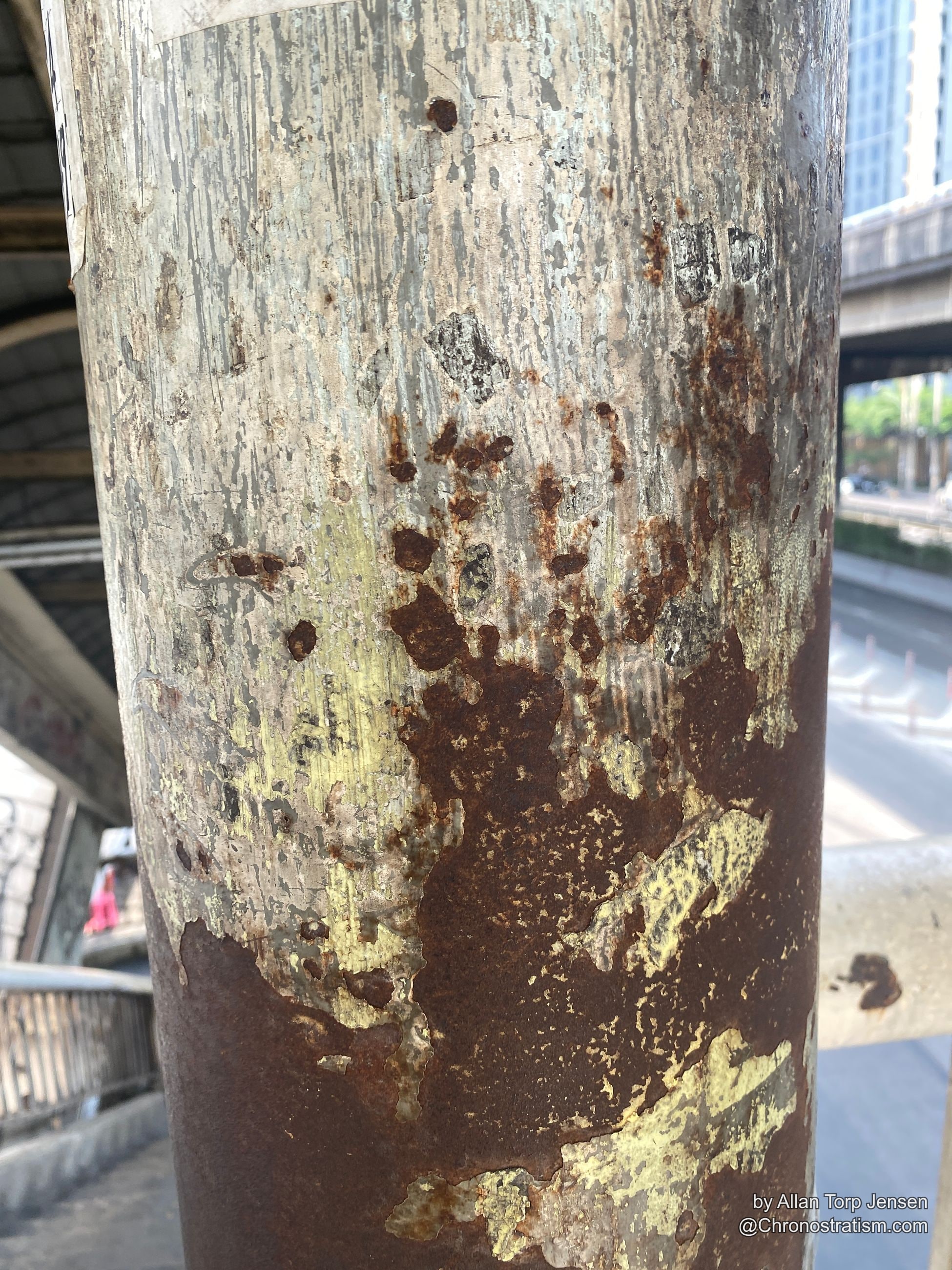 Rust patches spread across a metal railing over layers of white and yellow paint.