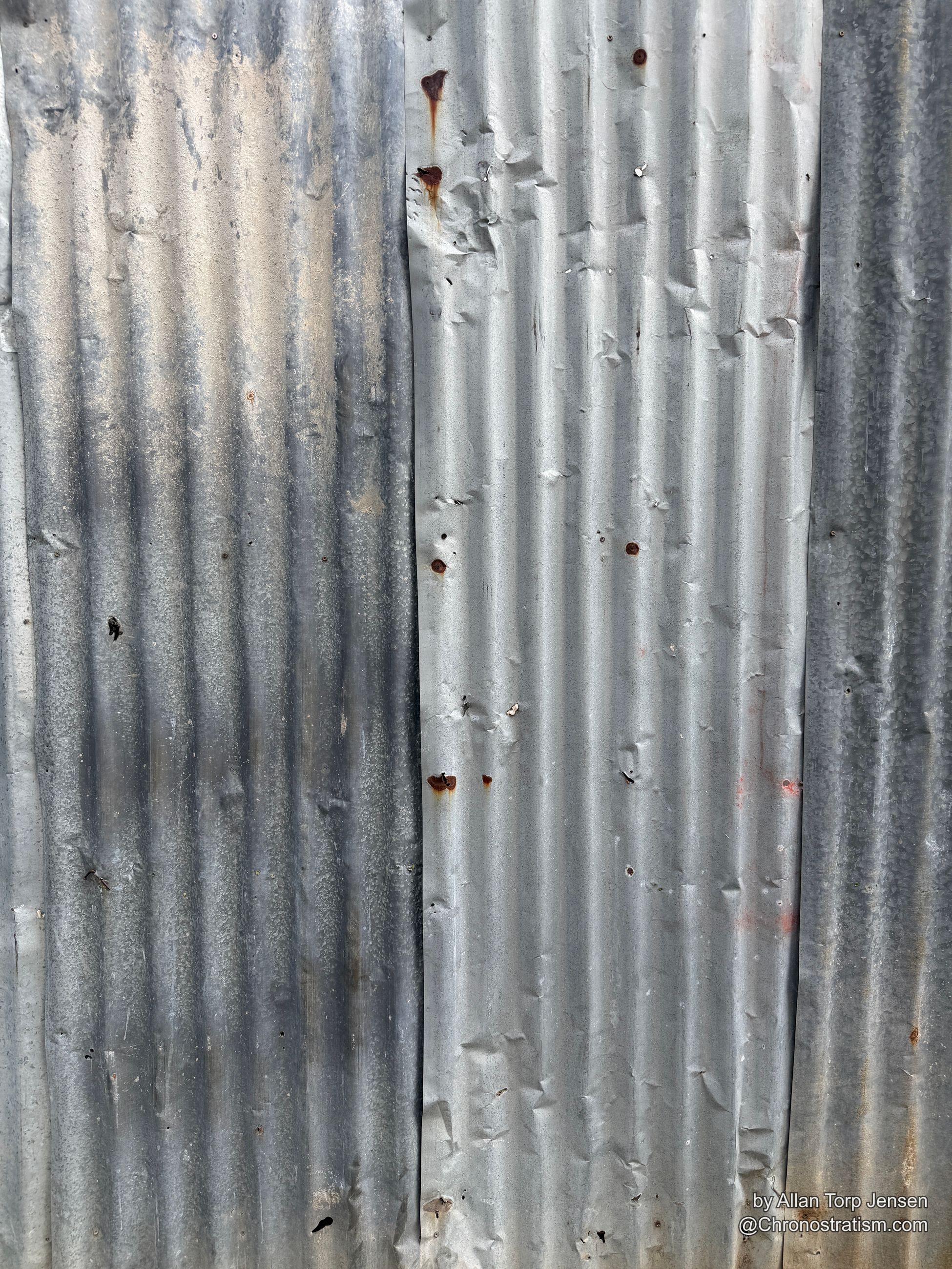 Small rust holes and spots freckle an otherwise clean galvanized panel.