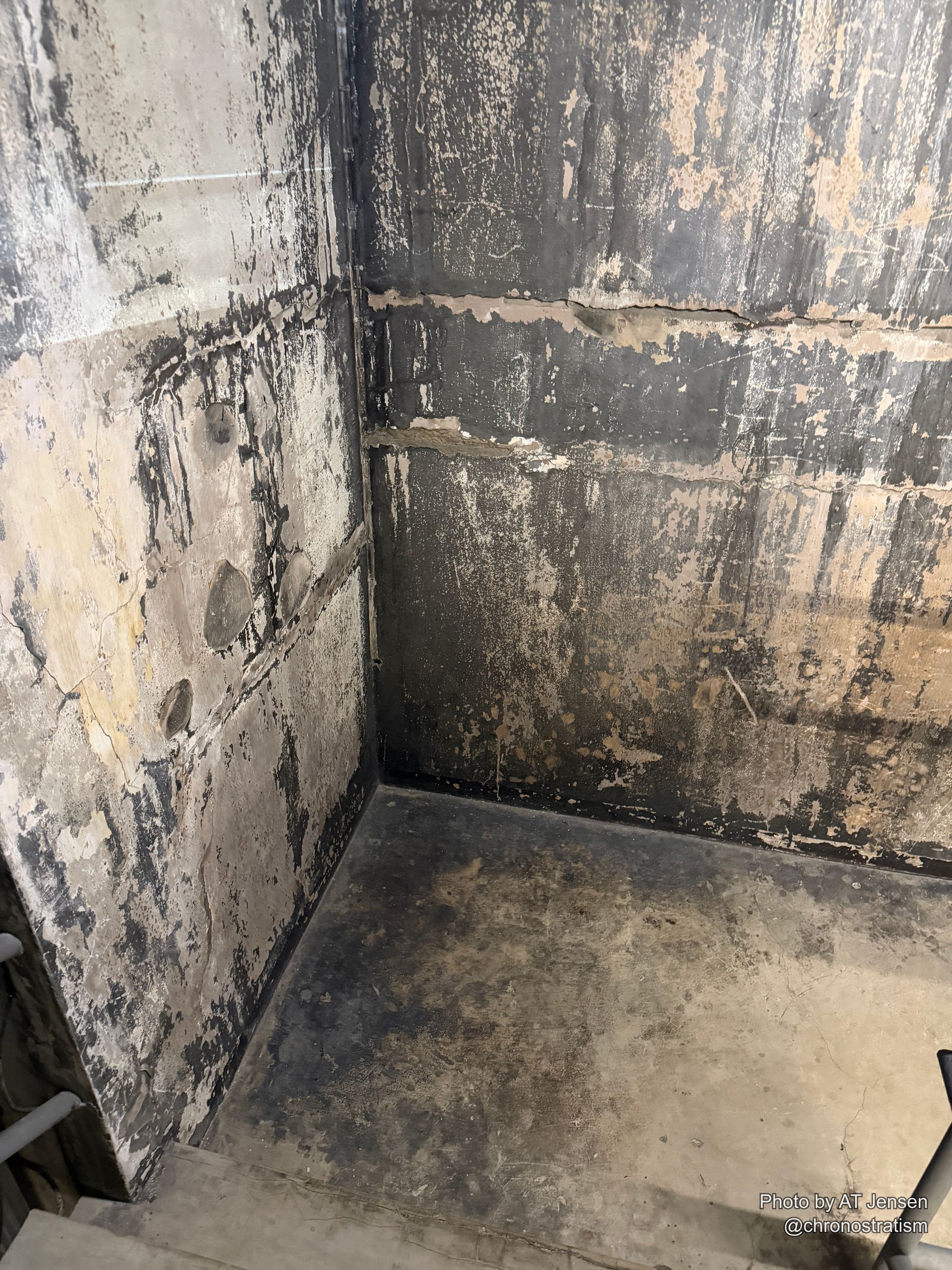 A soot-blackened interior corner meets the floor, exposed pipes running along the base of the wall.