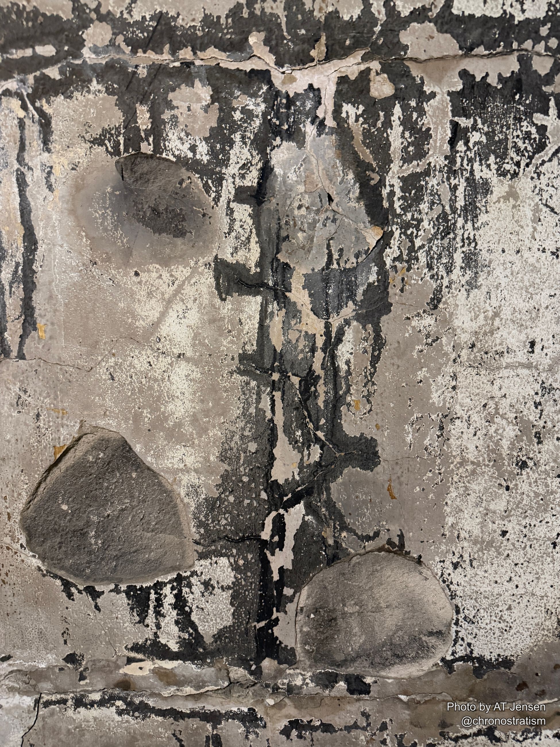Soot streaks down a concrete surface where two rounded aggregate stones sit exposed at the break.