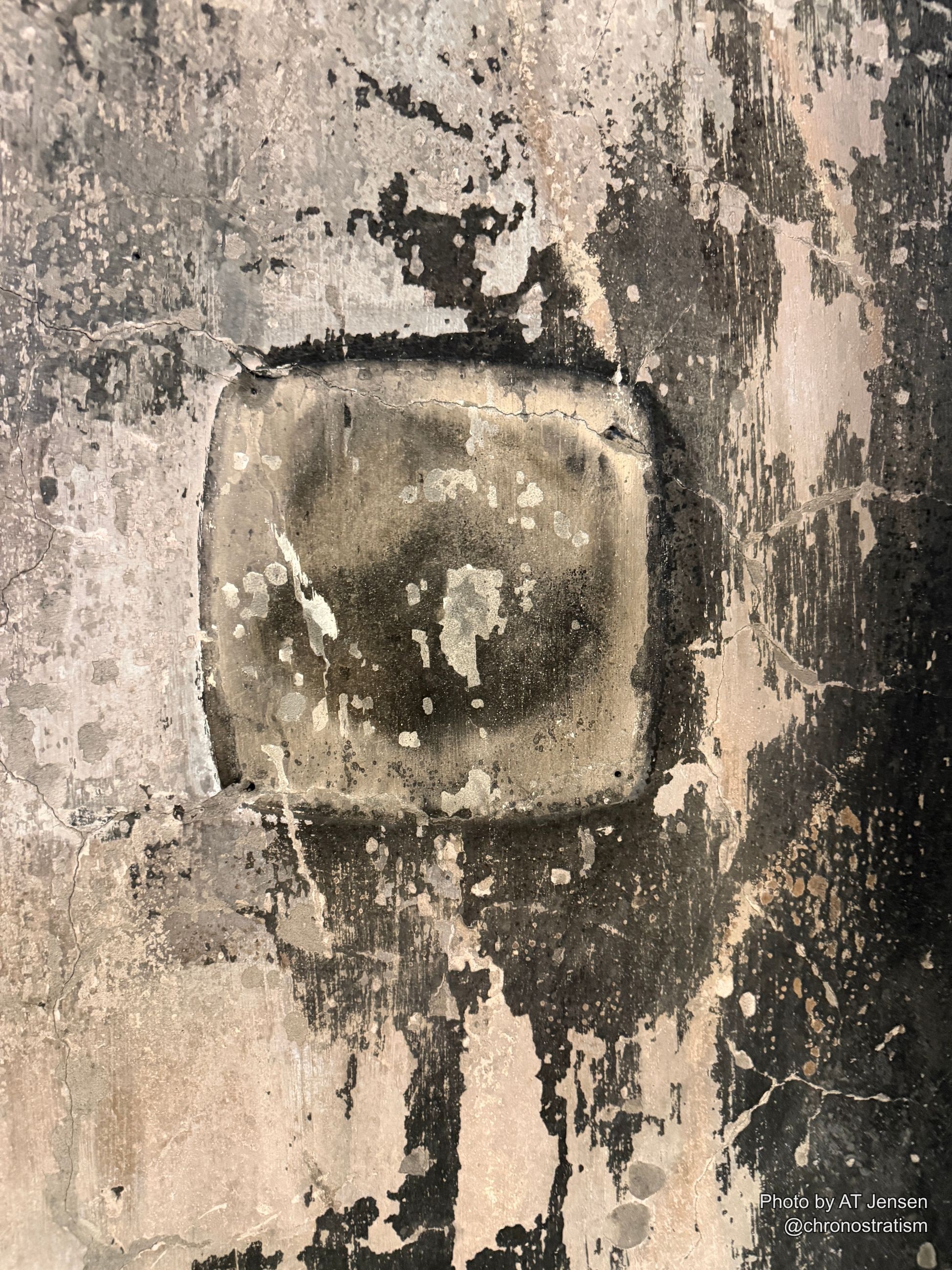 A rounded metal patch, heavily sooted, sits set into a cracked and crumbling render wall.