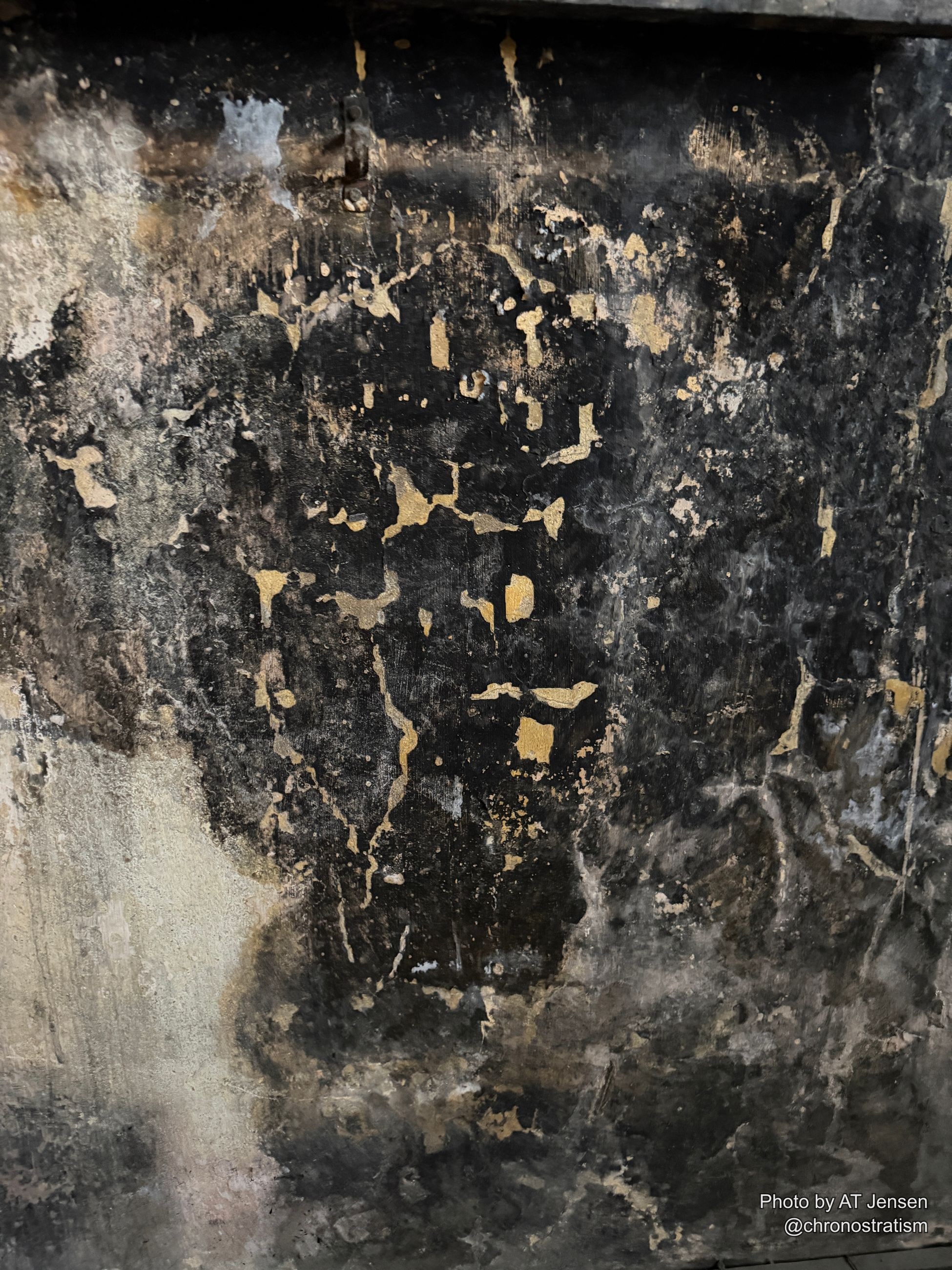 Gold paint flecks survive across a heavily sooted surface, a rusted latch set into the blackened wood.