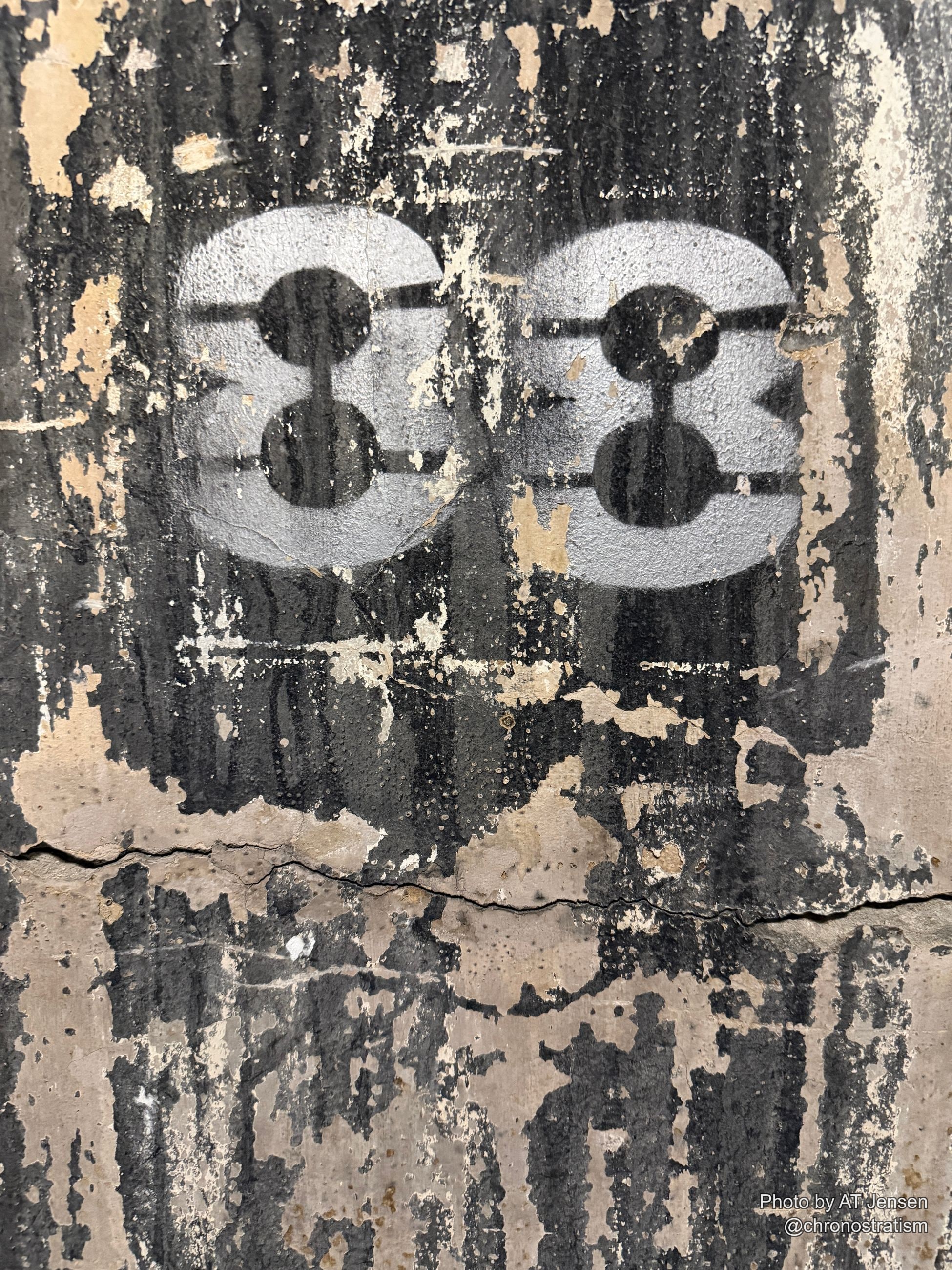 A pale stencilled glyph marks a soot-blackened, cracked wall.
