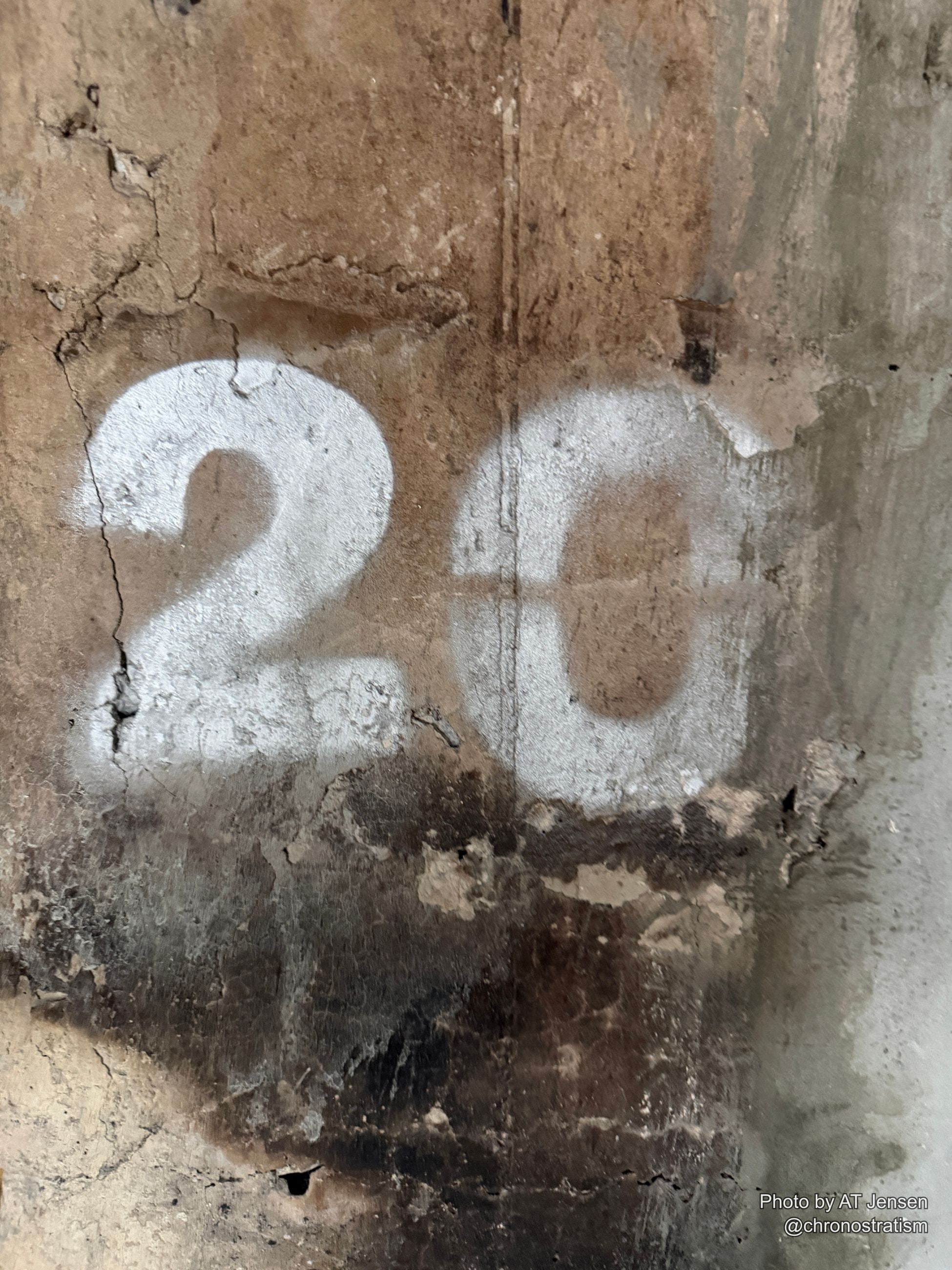 White stencilled numerals mark a grimy, stained wall, faint circular scrawl looping beside them.