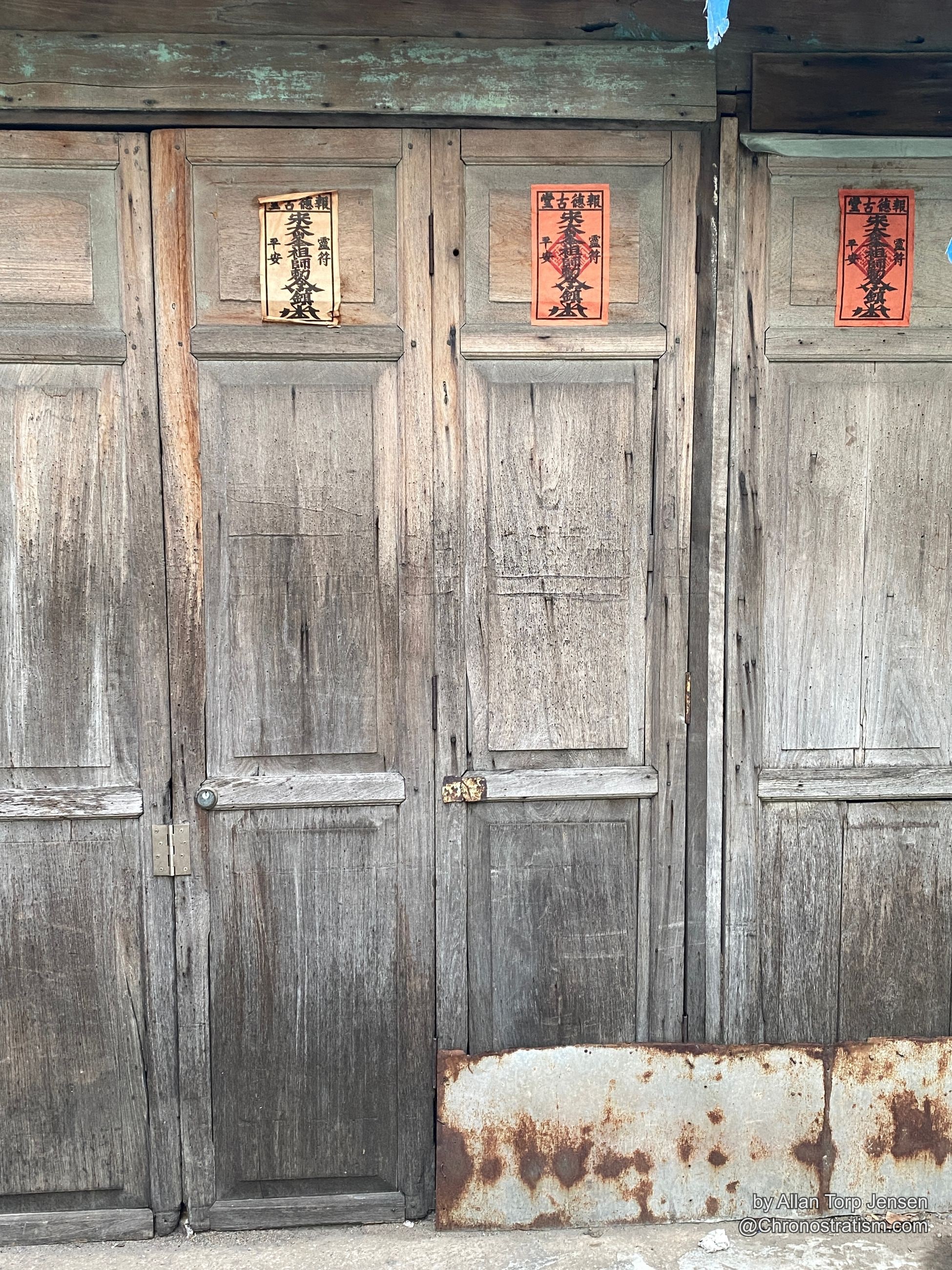 Three printed talisman papers repeat down a row of weathered carved door panels.