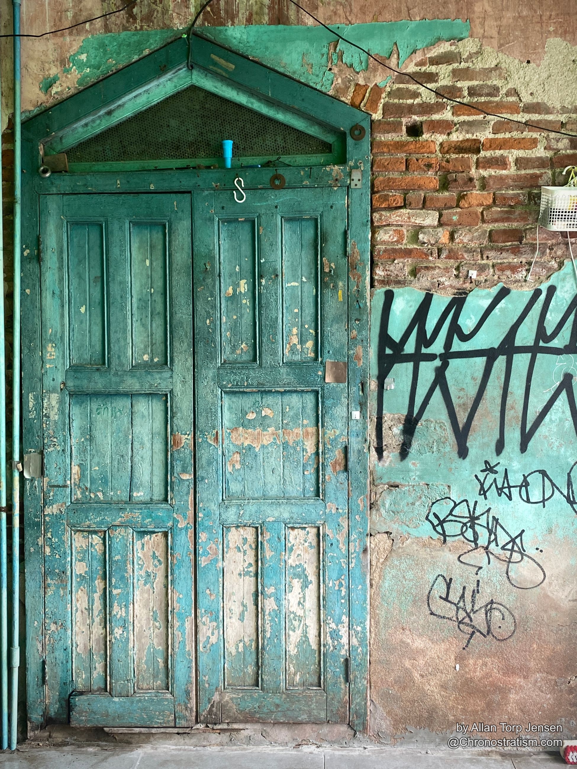 Weathered teal double doors peel in dramatic layers beside a graffiti-tagged brick wall.