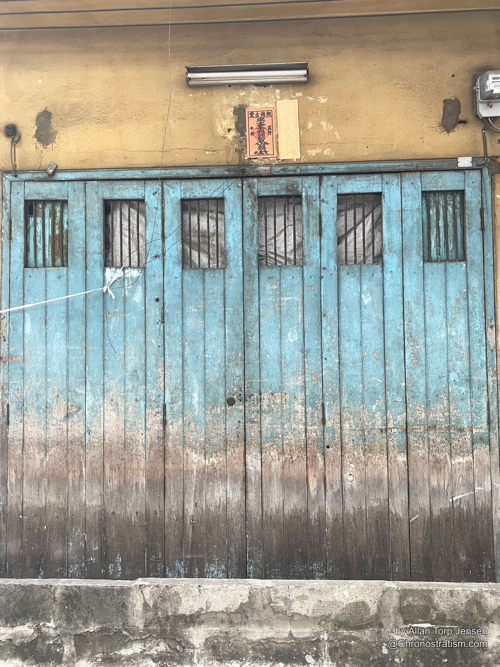 Weathered teal paint flaking off a slatted timber shutter, water staining across the boards.
