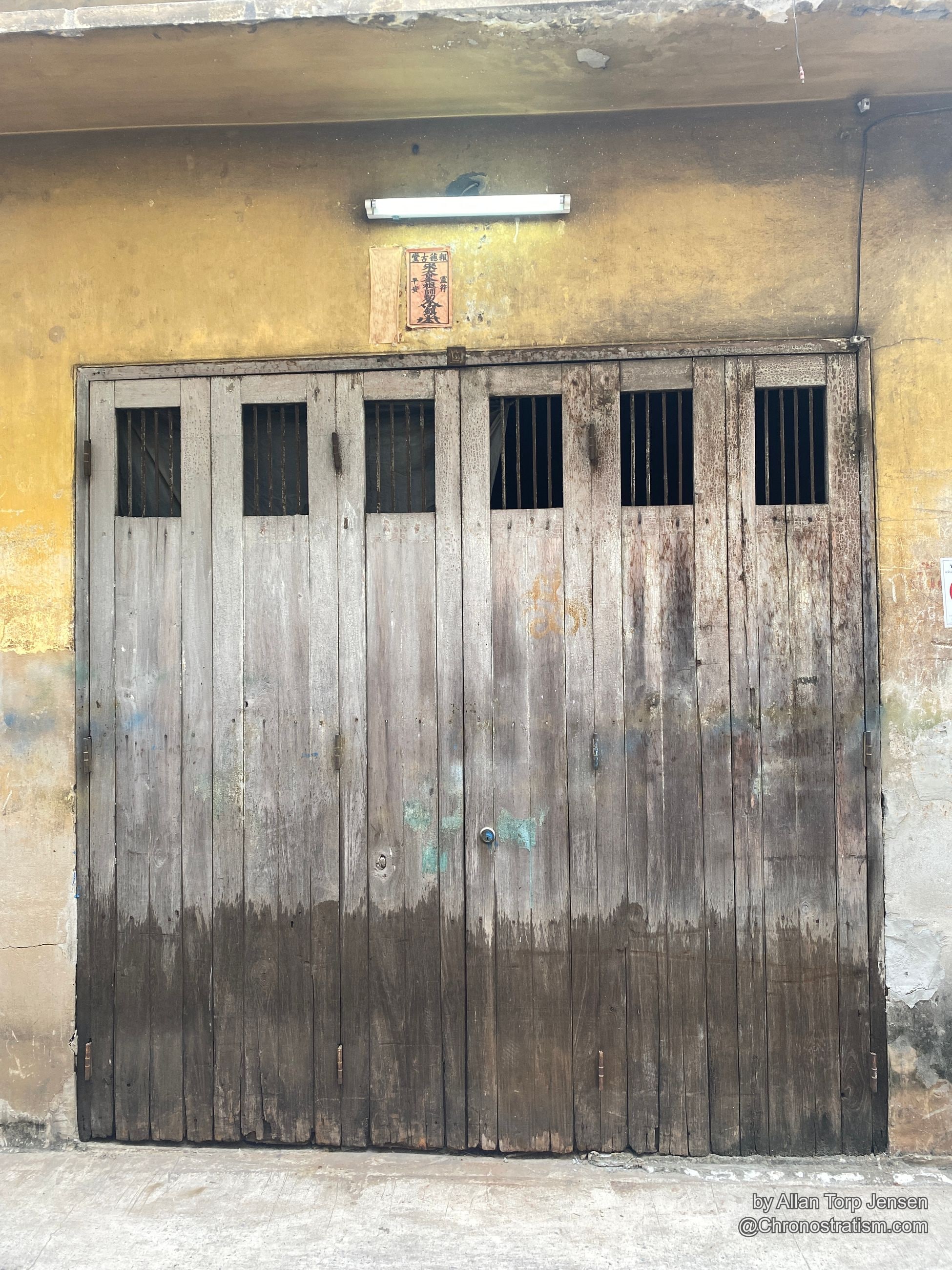A weathered wooden shutter splits sharply between dark stain and faded grey wood.