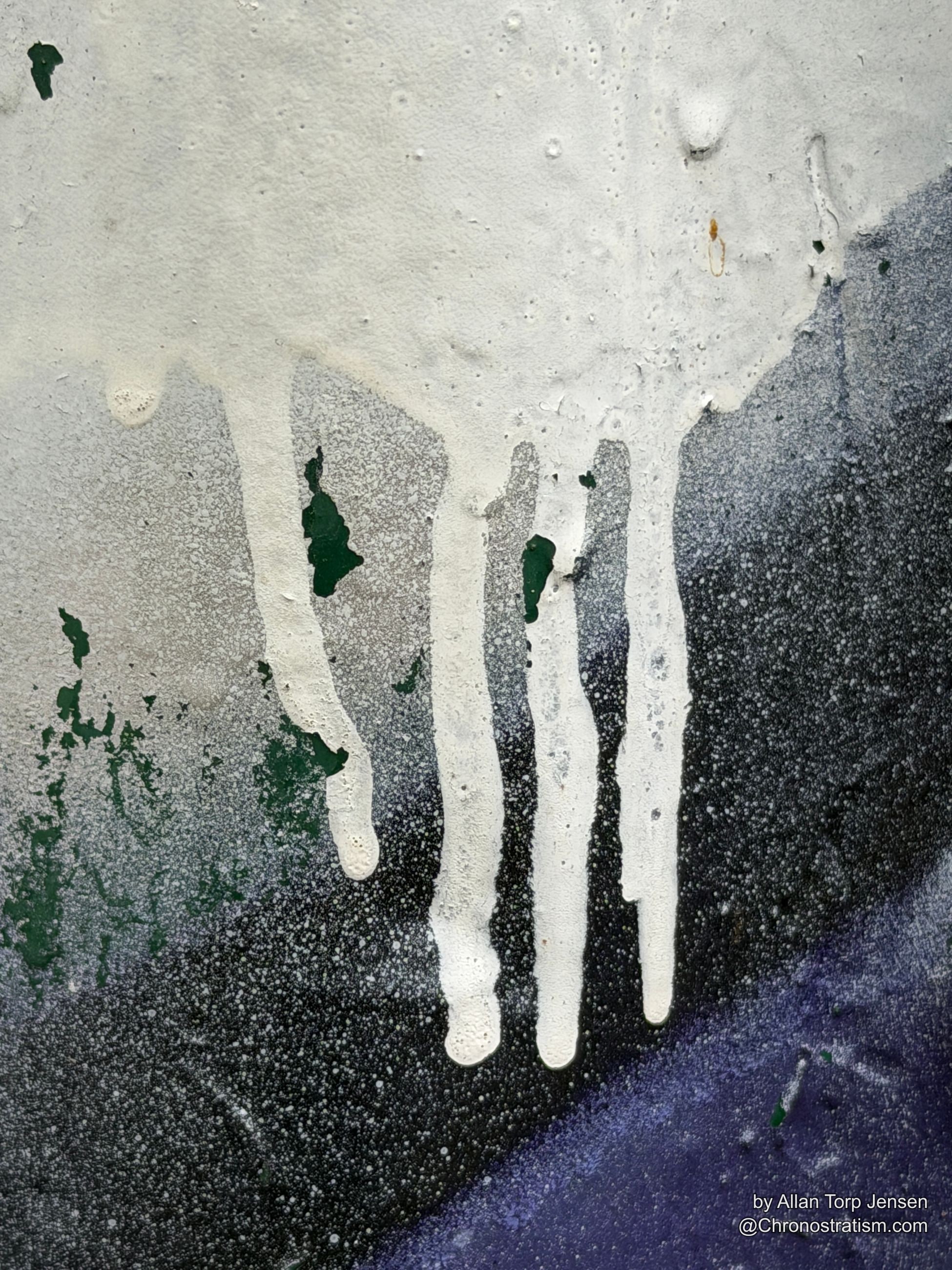 White and black spray paint drips in loose abstract pours down old signage.