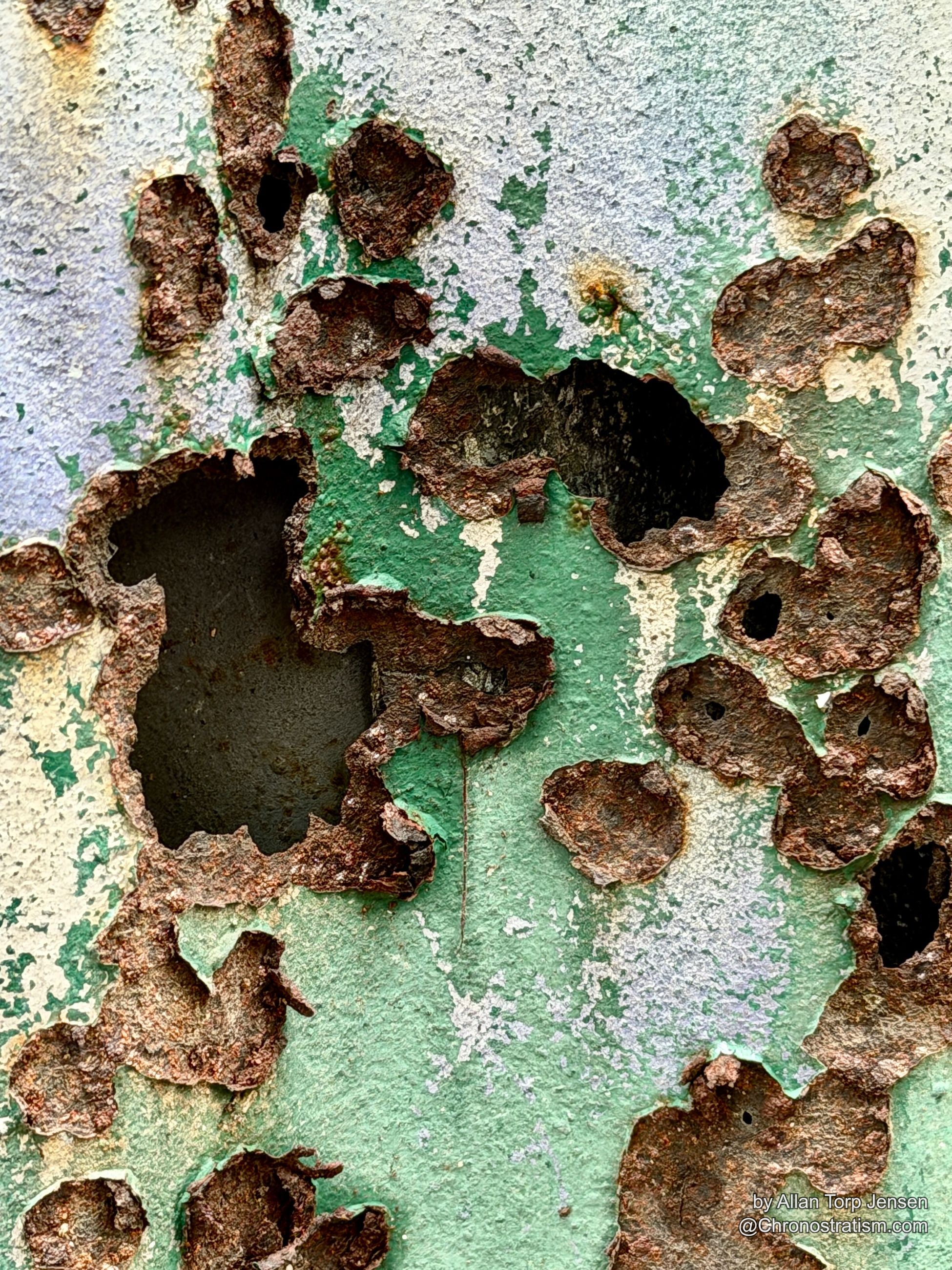 White paint gives way to a field of rust perforations on the same panel.
